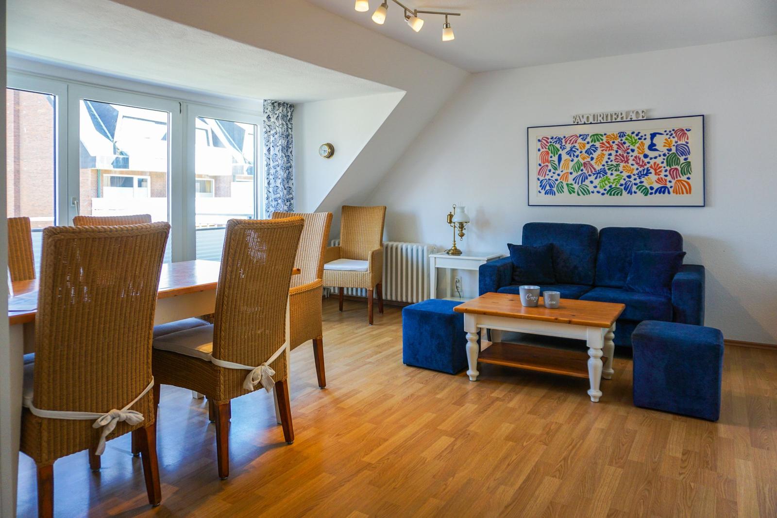 Living and dining area with blue sofa, wooden table, and wicker chairs.