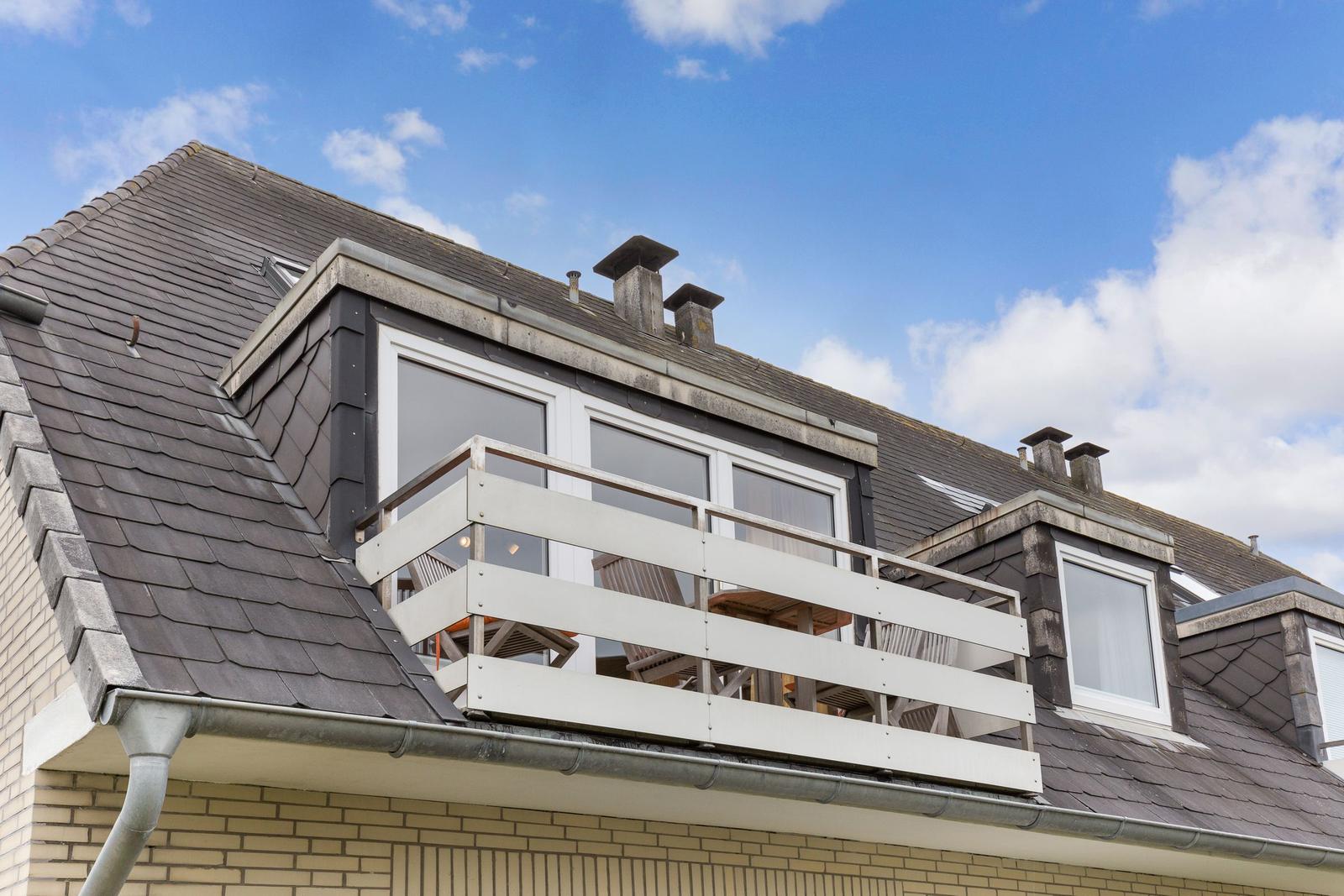 Attic with balcony and large windows under blue sky.