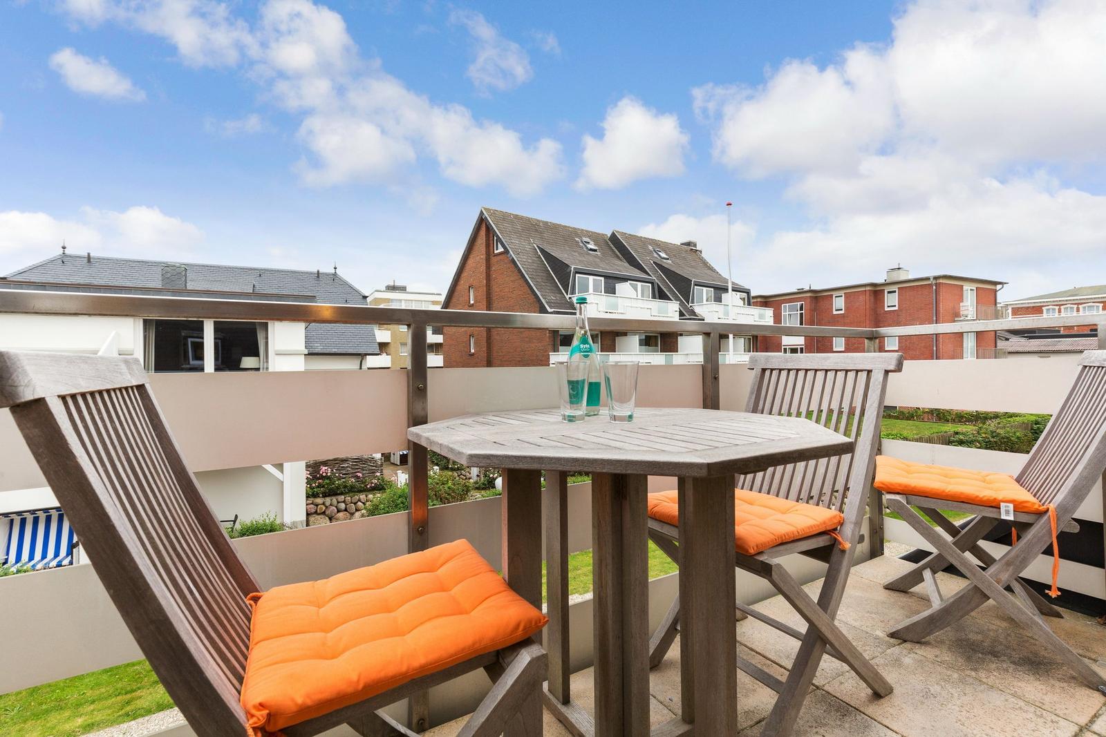 Terrace with wooden table and three chairs with orange cushions.