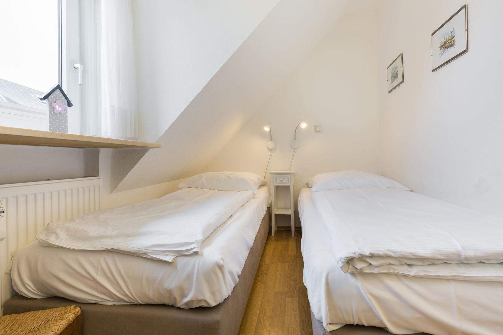 Two single beds under sloped ceiling with window and nightstand.