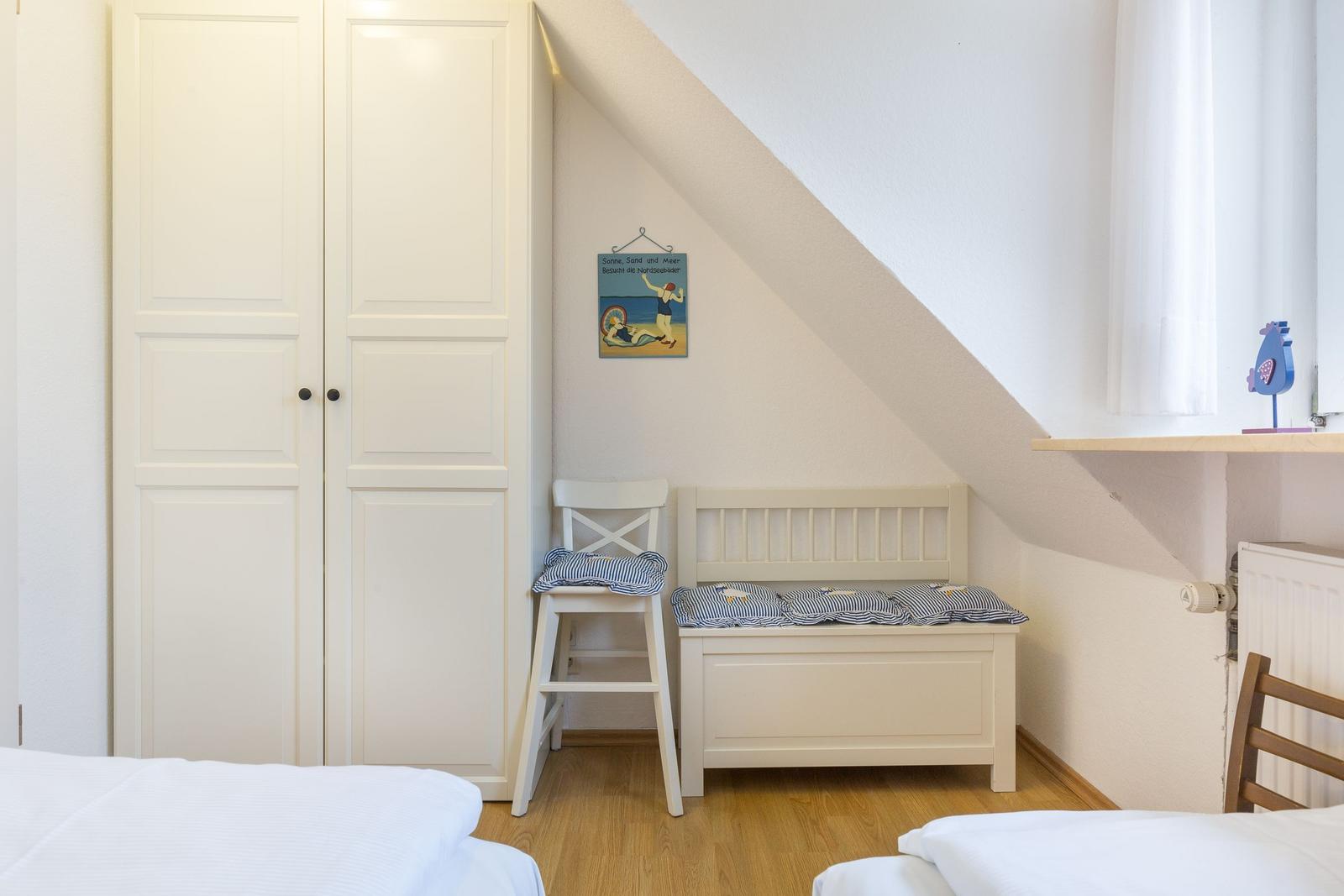 Room with sloped ceiling, wardrobe, chair, and bench with cushions.