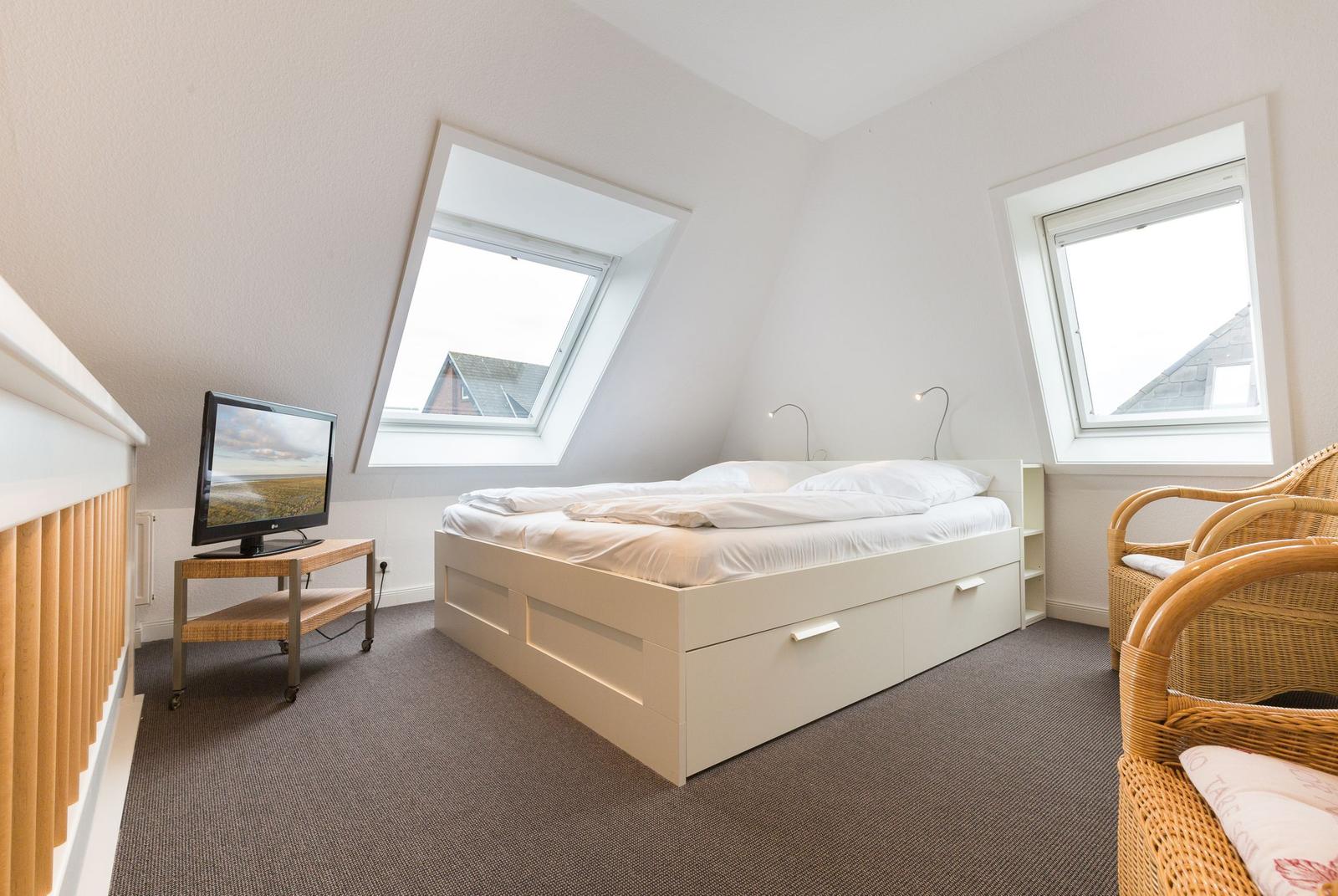 Bedroom with sloped ceiling, bed, TV, and two windows.