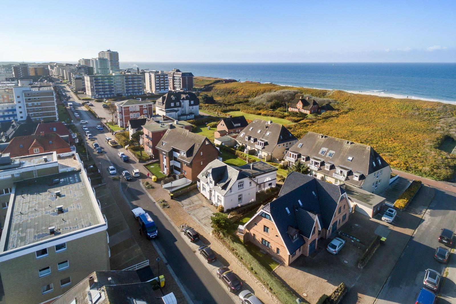 Aerial view of coastal town with houses, streets, and ocean in background.
