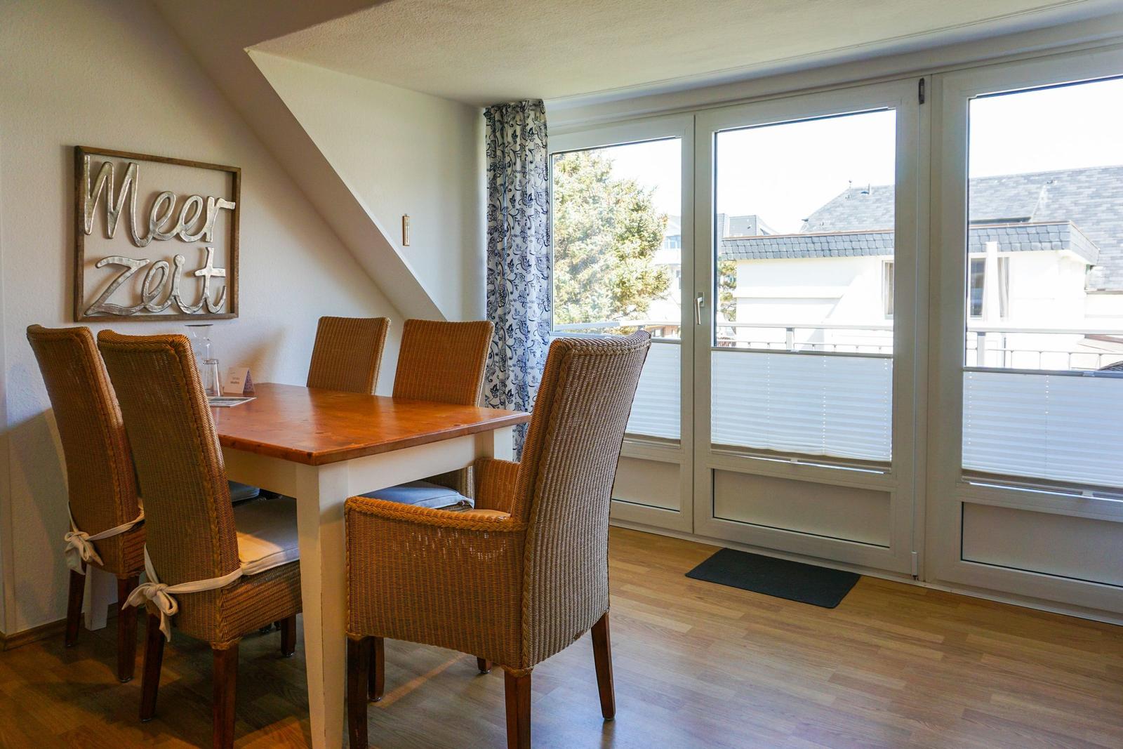 Dining area with table and chairs, view to balcony through windows.