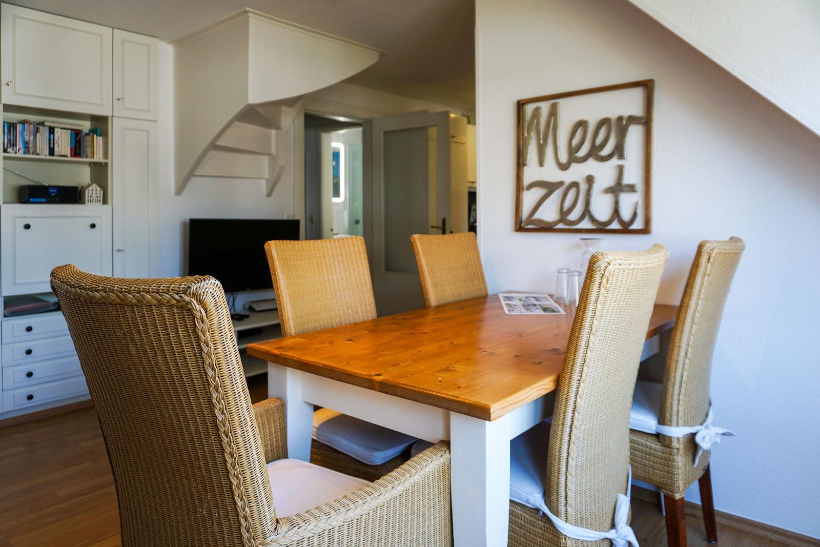 Dining room with wooden table, rattan chairs, and wall art Meer Zeit