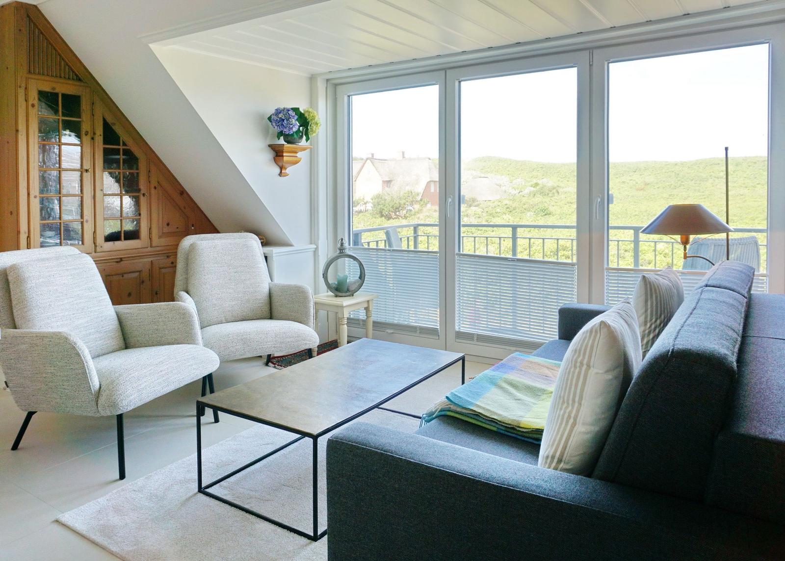 Wohnzimmer mit Sofa, zwei Sesseln und Blick auf Balkon.