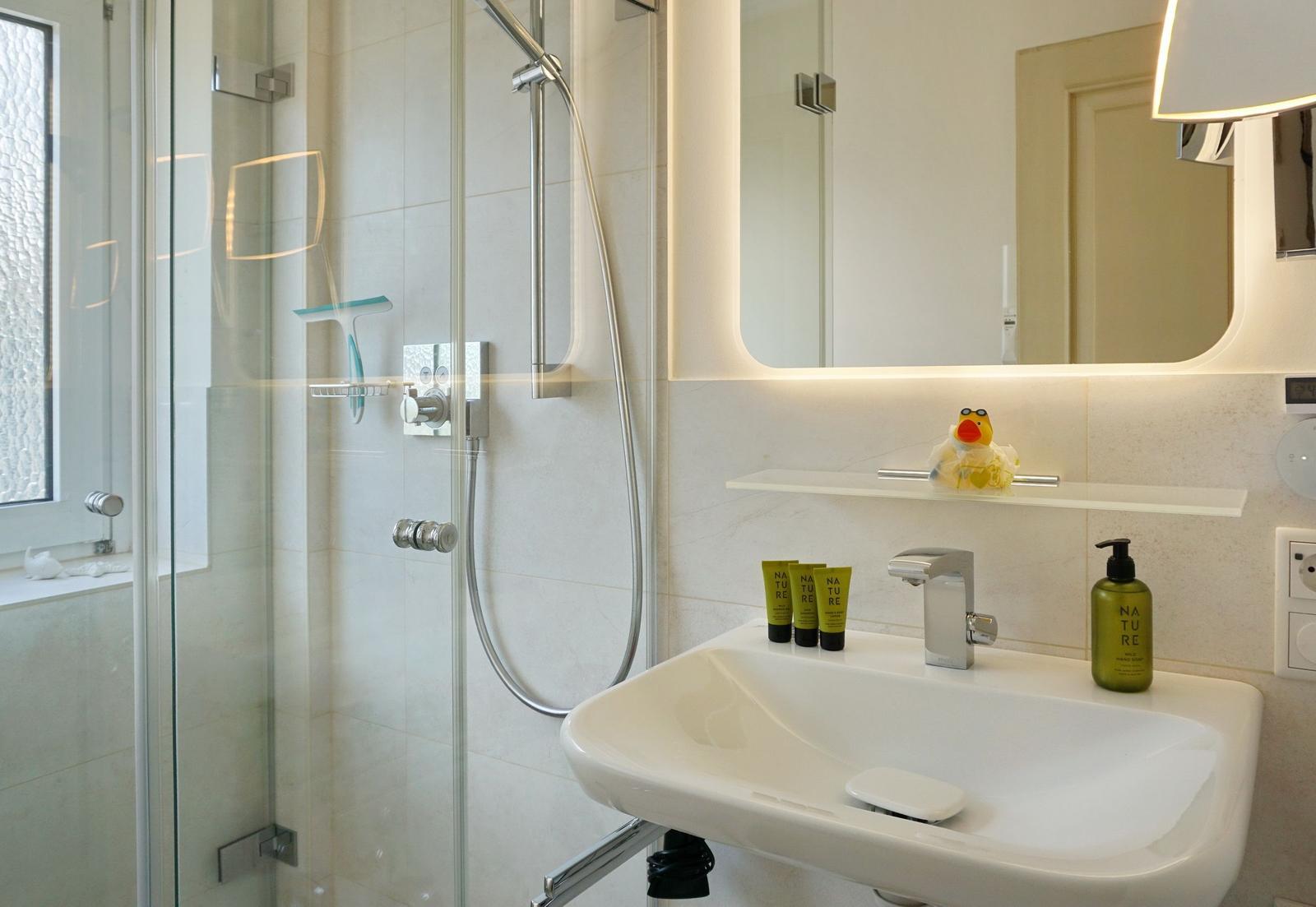Bad mit Dusche, Waschbecken und Spiegel mit Beleuchtung.