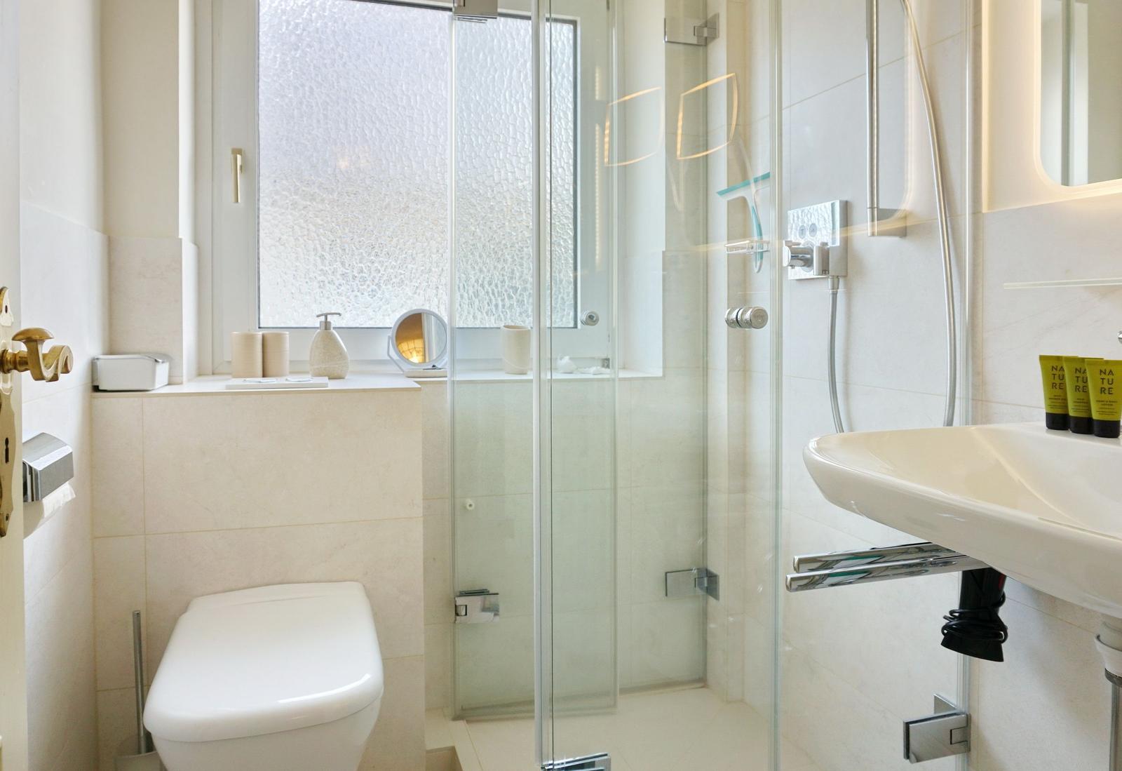 Bad mit Dusche, Waschbecken und Toilette. Fenster mit getöntem Glas.