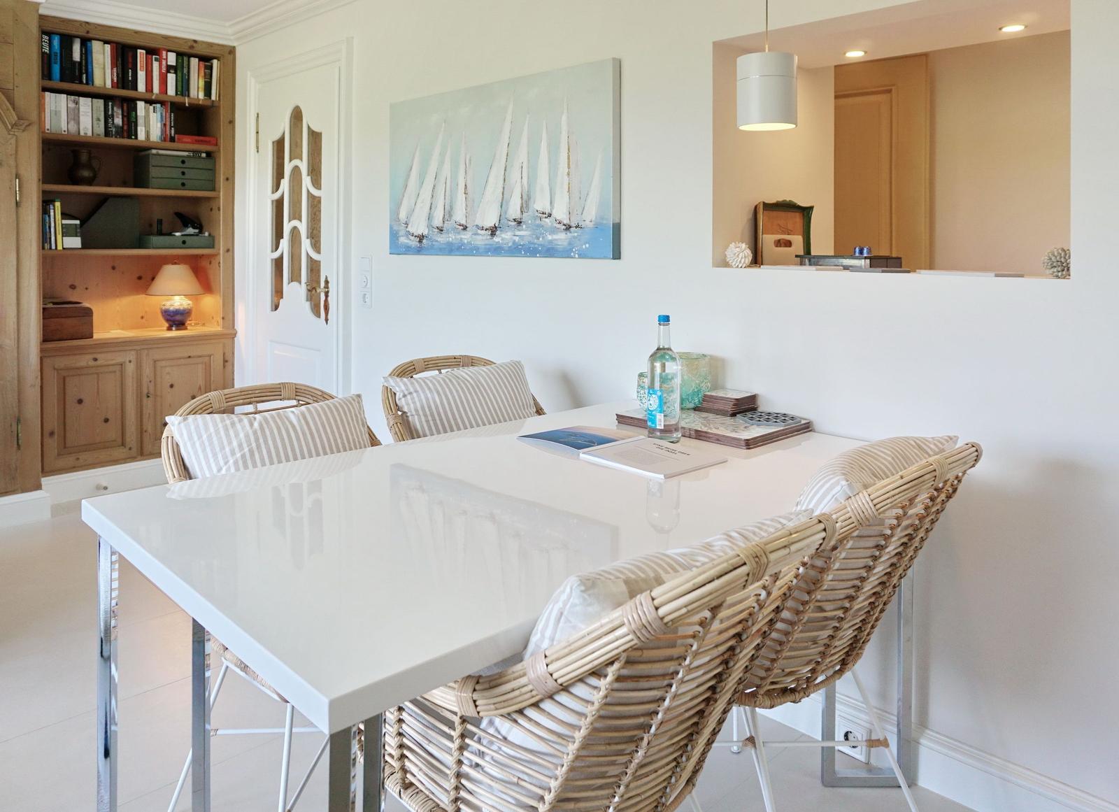 Esstisch mit vier Rattan-Stühlen und Wandbild mit Segelbooten.