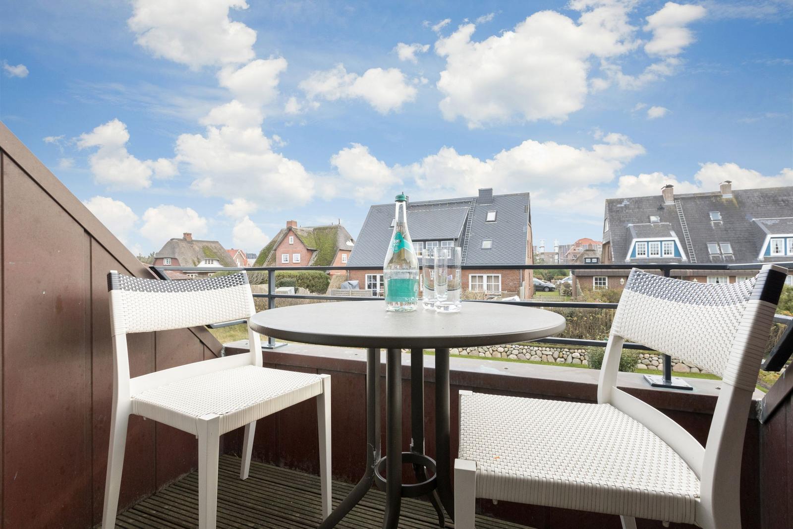 Terrasse mit Tisch und zwei Stühlen. Blick auf Dächer und Himmel.
