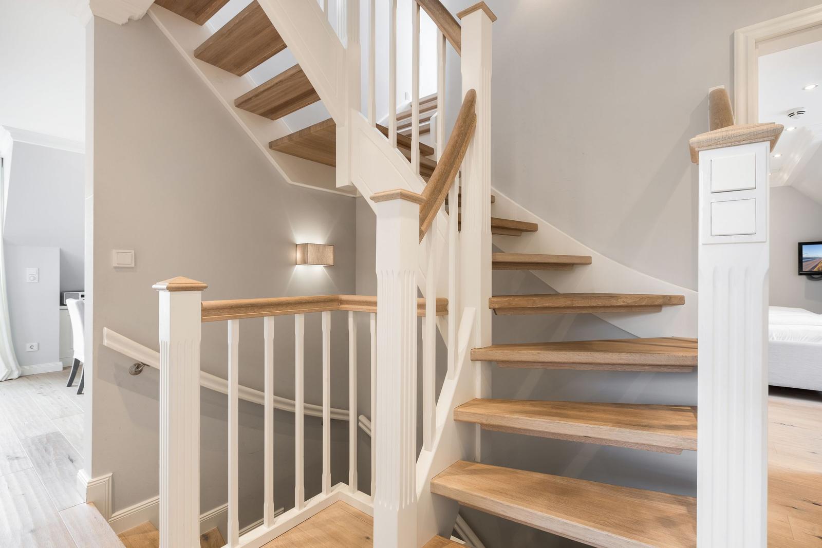 Holzgetriebene Treppe mit weißem Geländer führt zu einer oberen Etage.