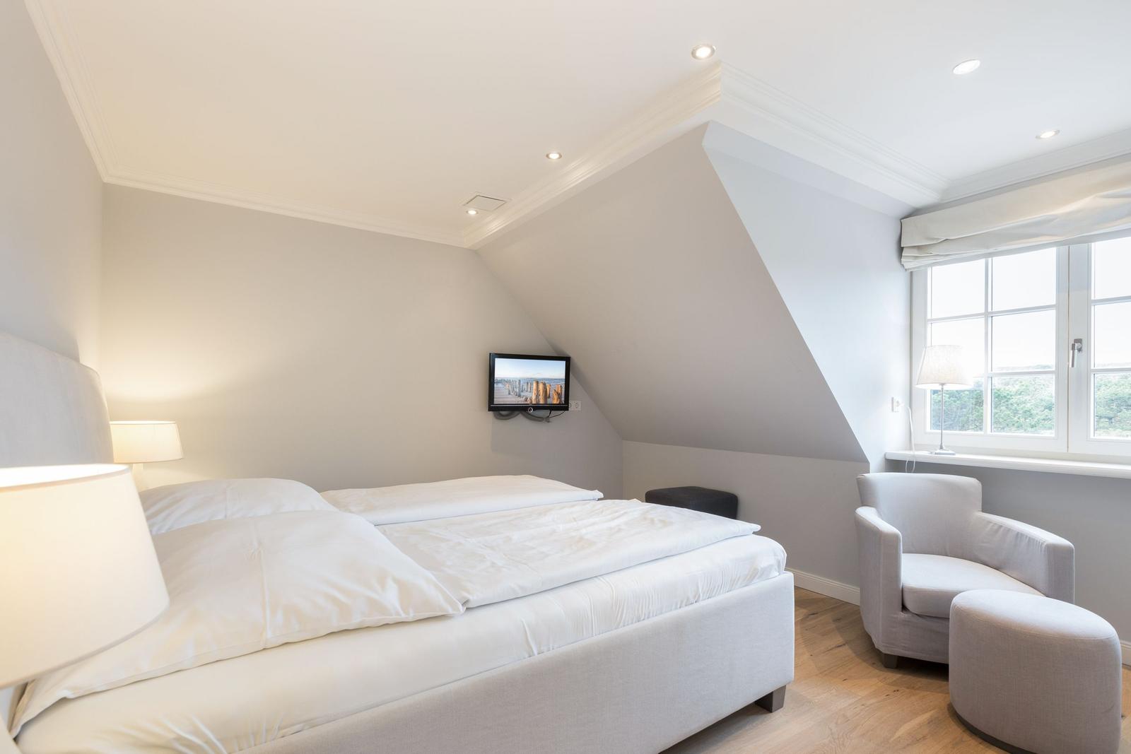 Schlafzimmer mit Doppelbett, Sessel und Fenster.