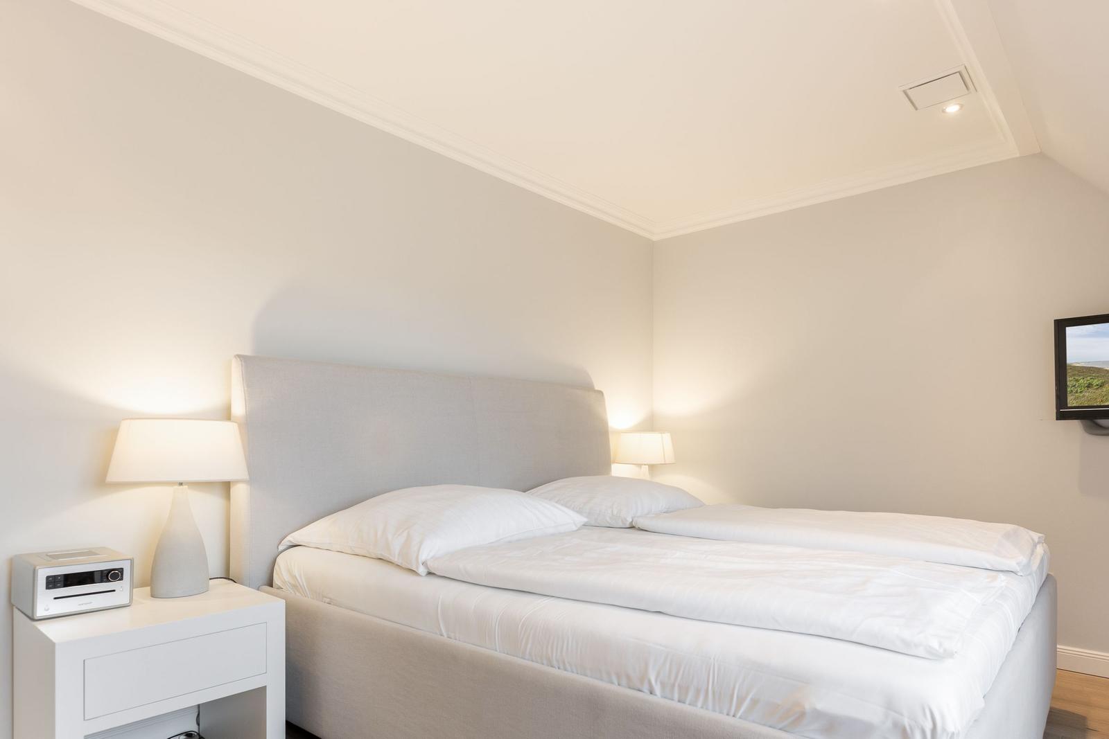 Schlafzimmer mit Doppelbett, Nachttisch und Wandfernseher.