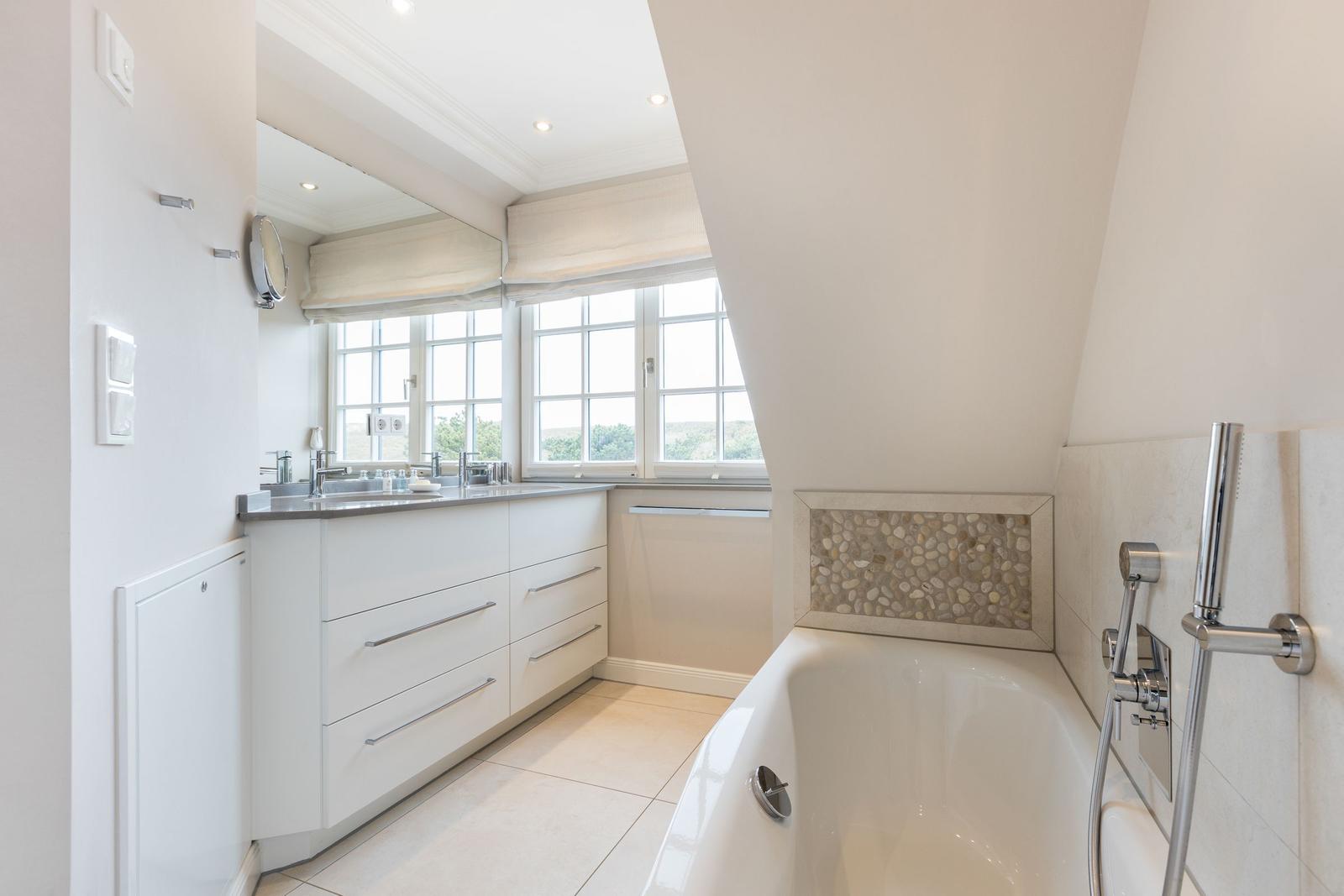 Badezimmer mit Badewanne, Waschbecken und Fenstern.