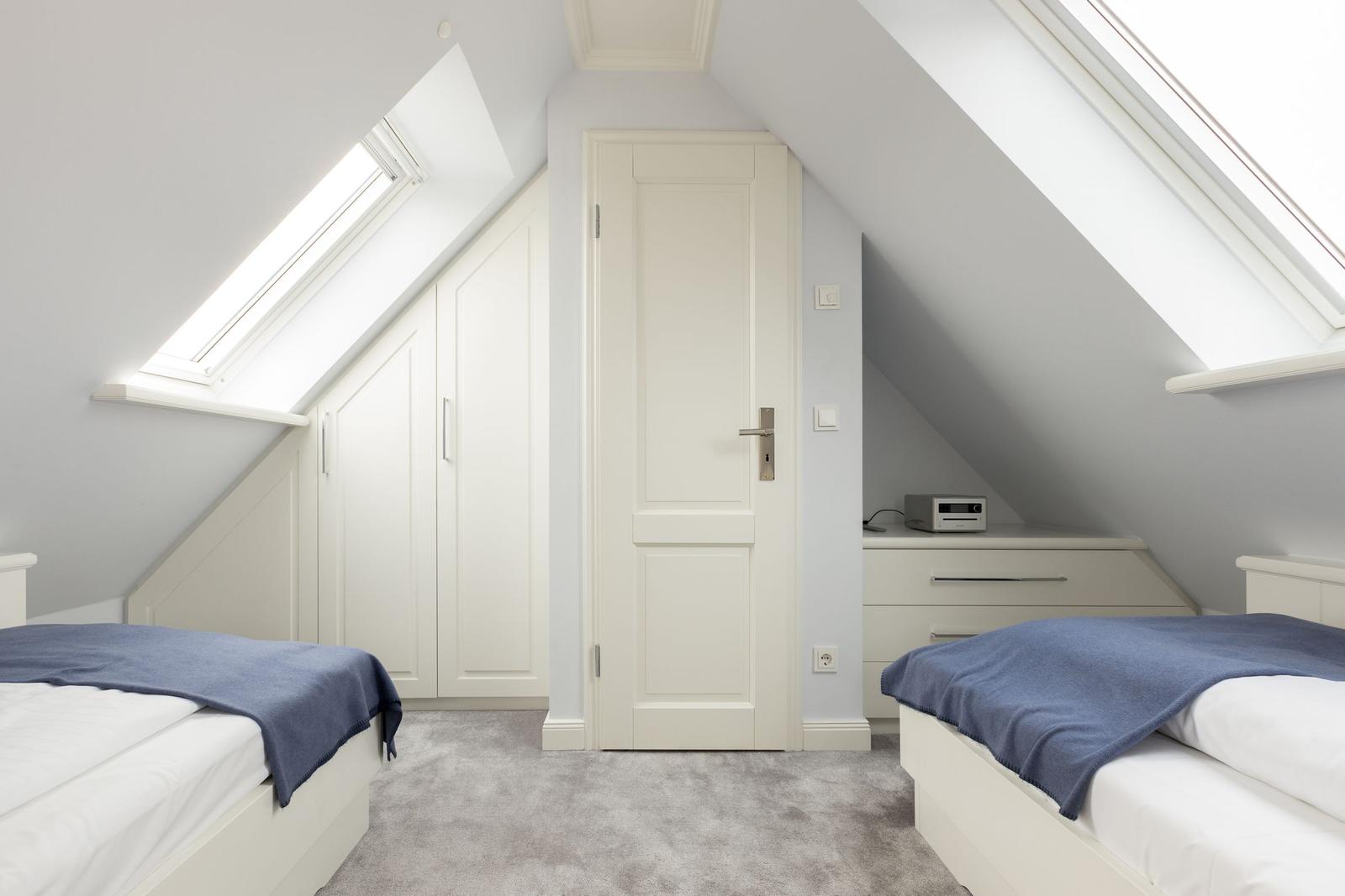 Zimmer mit zwei Betten, Dachschrägen, Fenstern und Schränken.