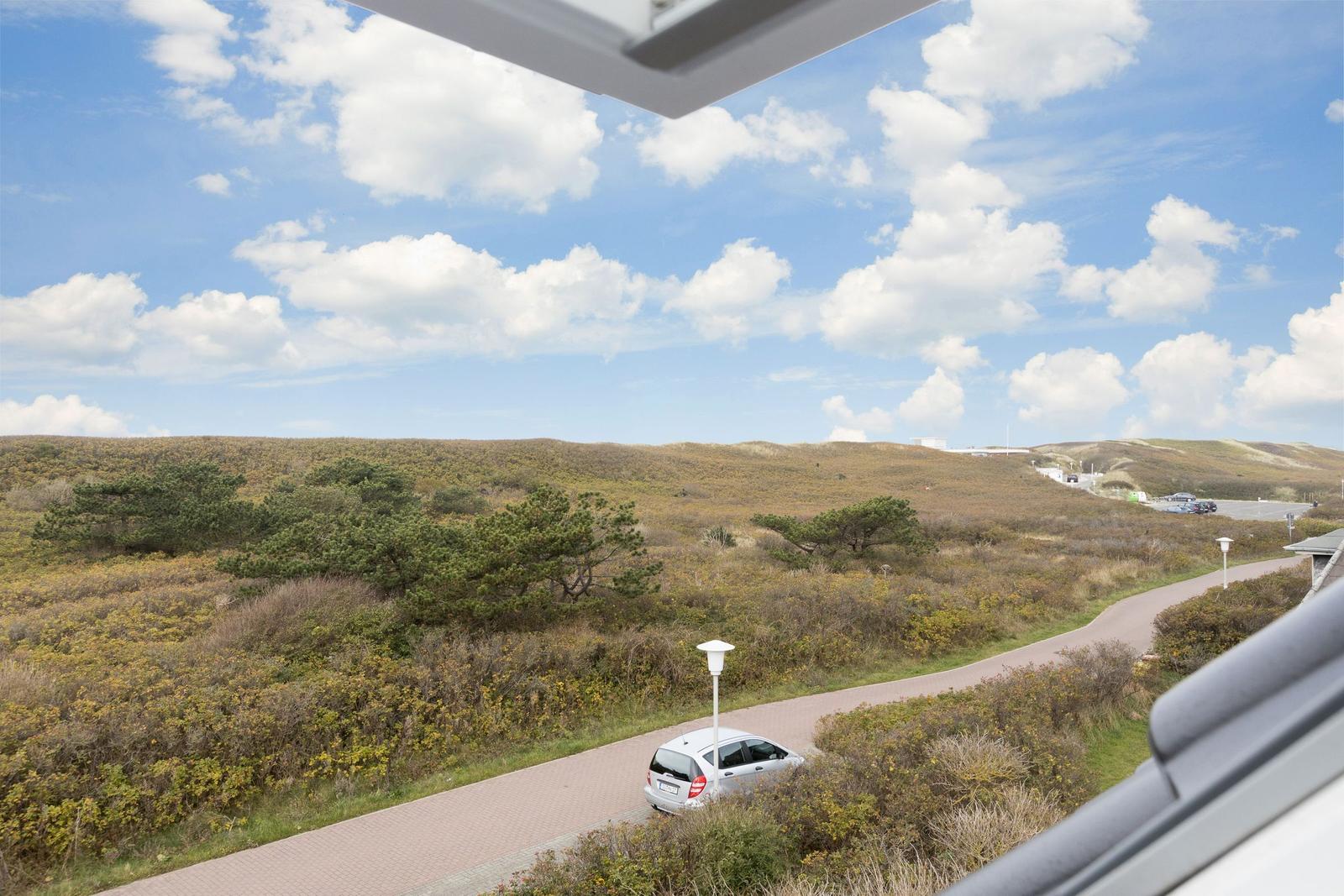 Dachterrasse mit Blick auf grüne Hügel und einen gepflasterten Weg mit einem weißen Auto.