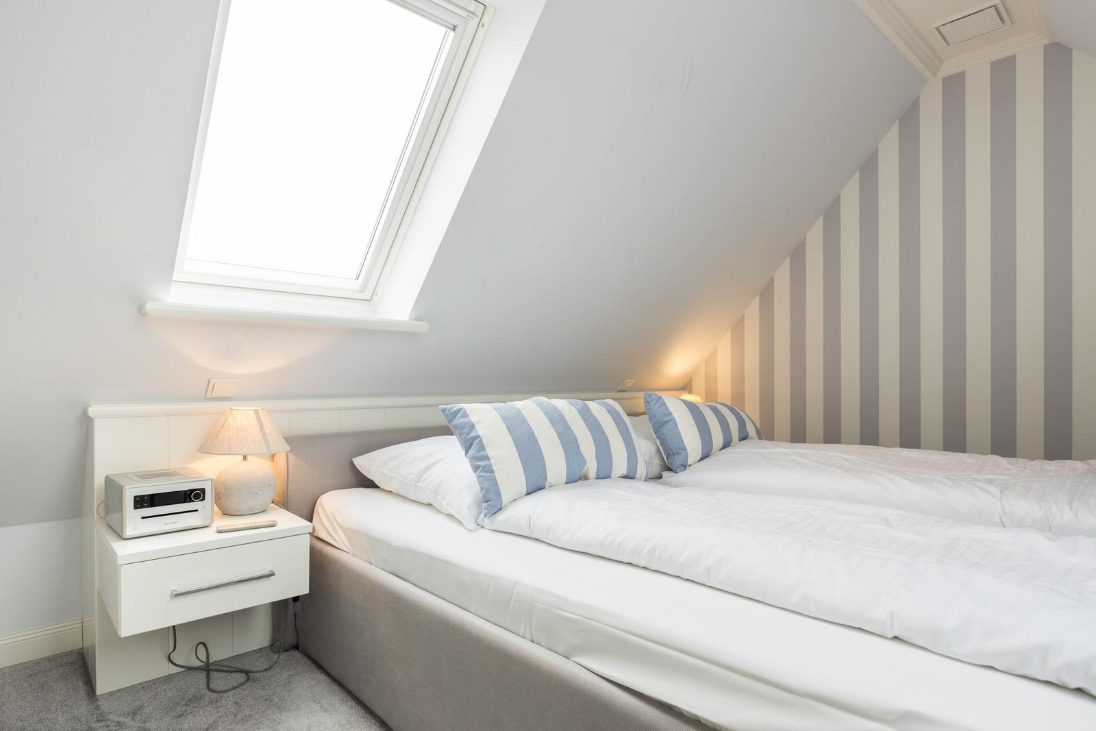 Schlafzimmer mit Dachfenster, gestreifter Wand und weißem Bett.