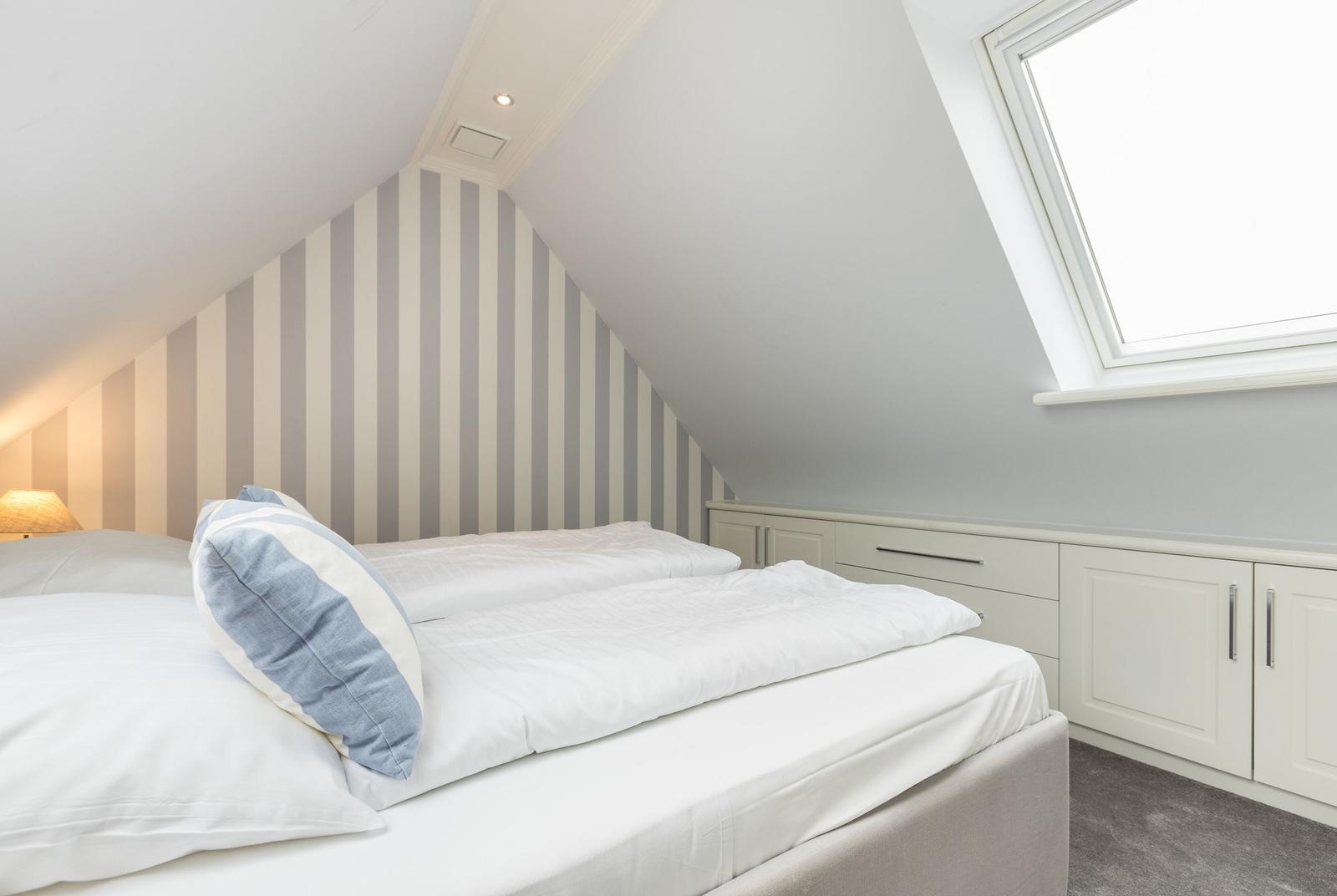 Schlafzimmer mit Dachschräge, gestreifter Wand und Dachfenster.