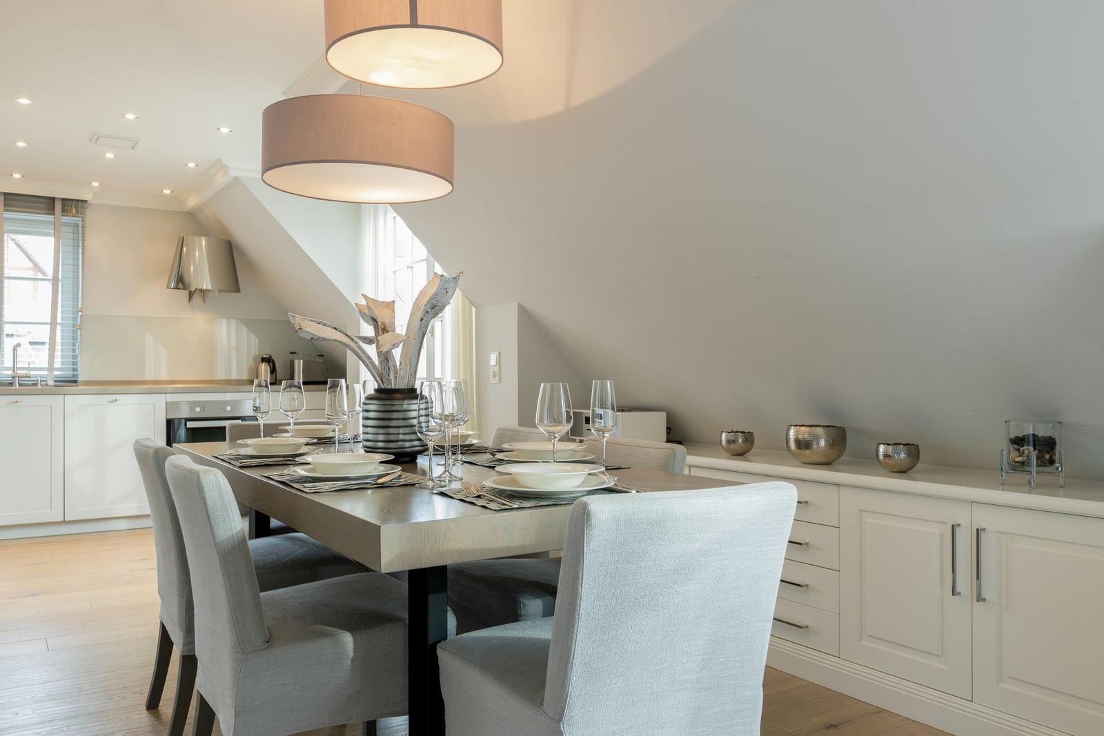 Essbereich mit Tisch, Stühlen und Deckenleuchten. Küche im Hintergrund.