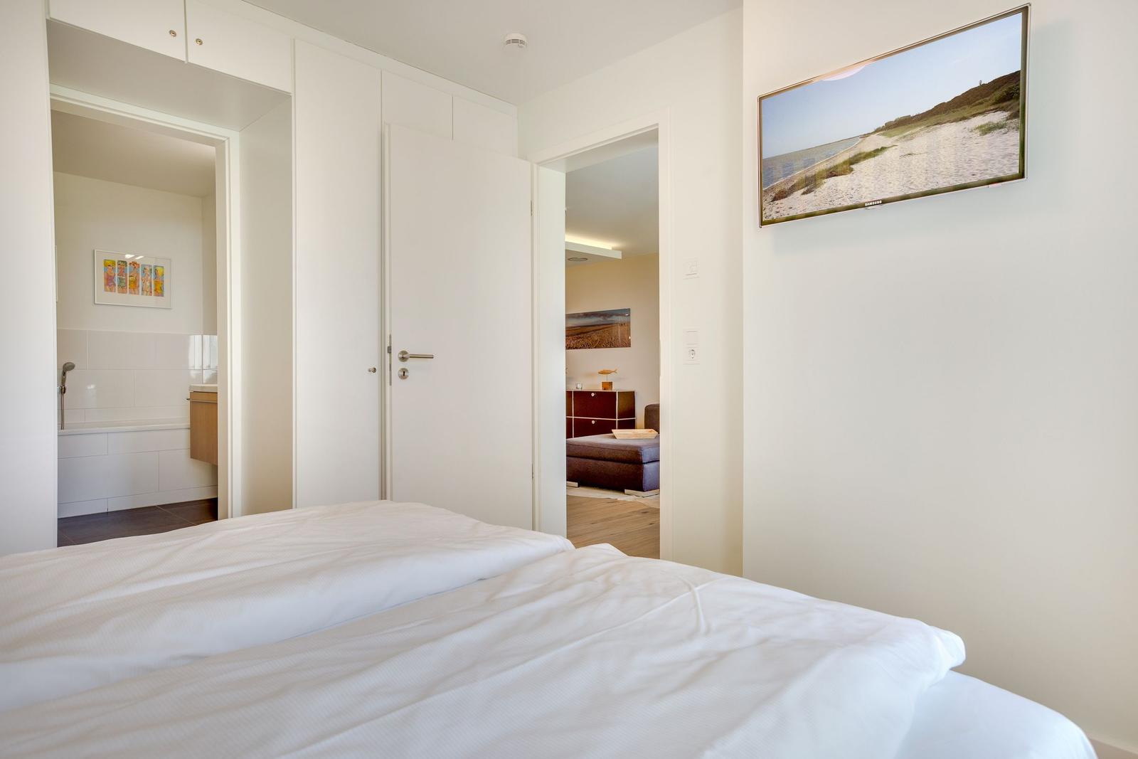 Schlafzimmer mit Bett, Bad und Wohnbereich. Wandbild zeigt Strand.