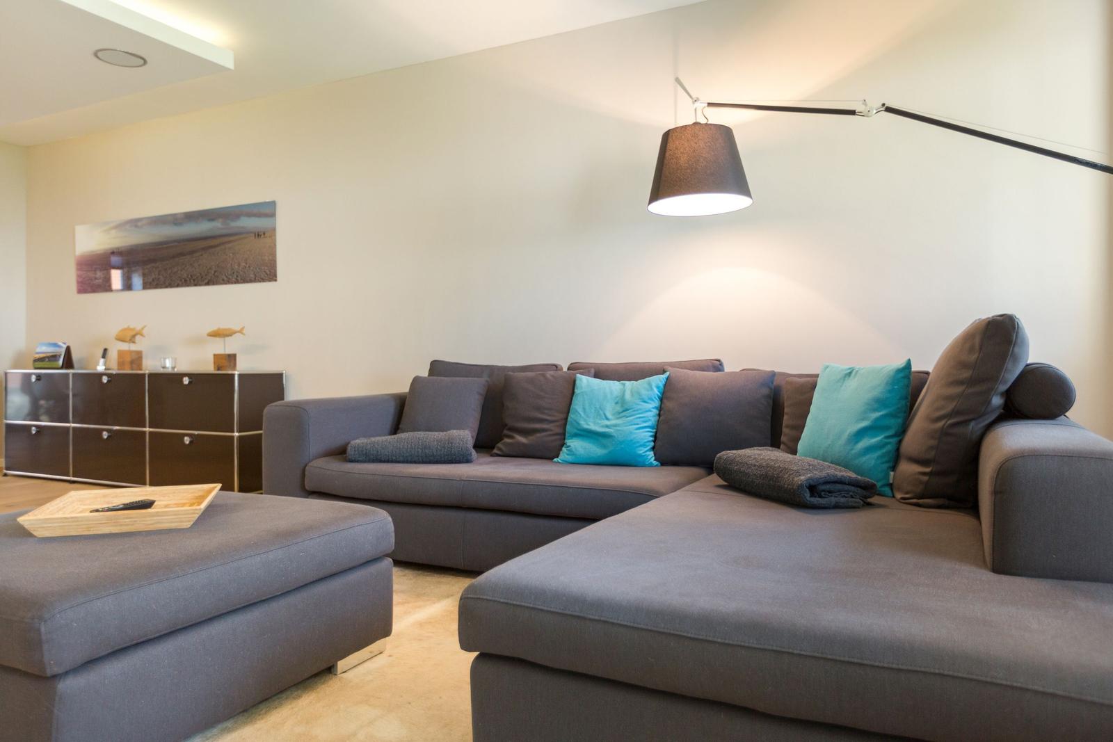 Ein Wohnzimmer mit grauem Sofa, blauen Kissen und einer Stehlampe.