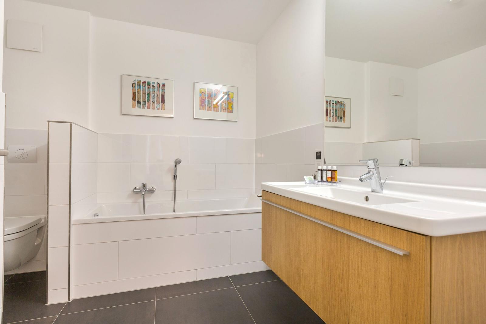 Badezimmer mit Badewanne, Waschbecken und Toilette. Wandbilder und Holzschränke.