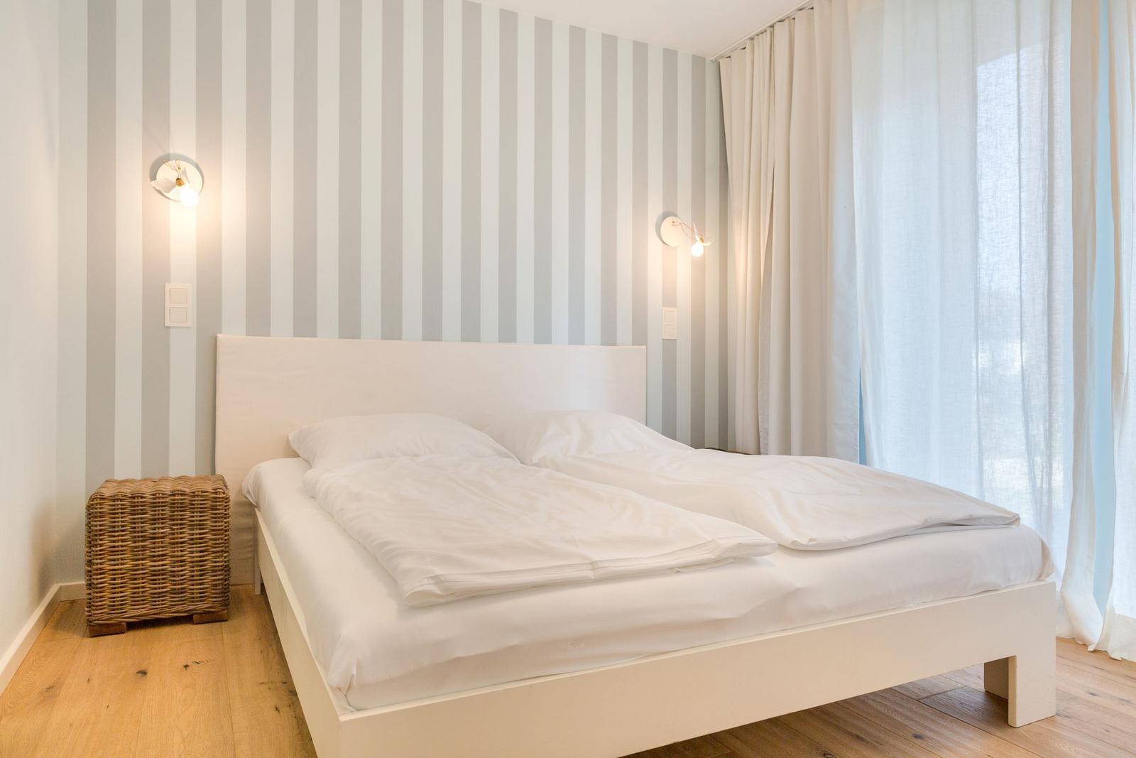 Schlafzimmer mit weißem Bett, gestreifter Wand und Holzboden.