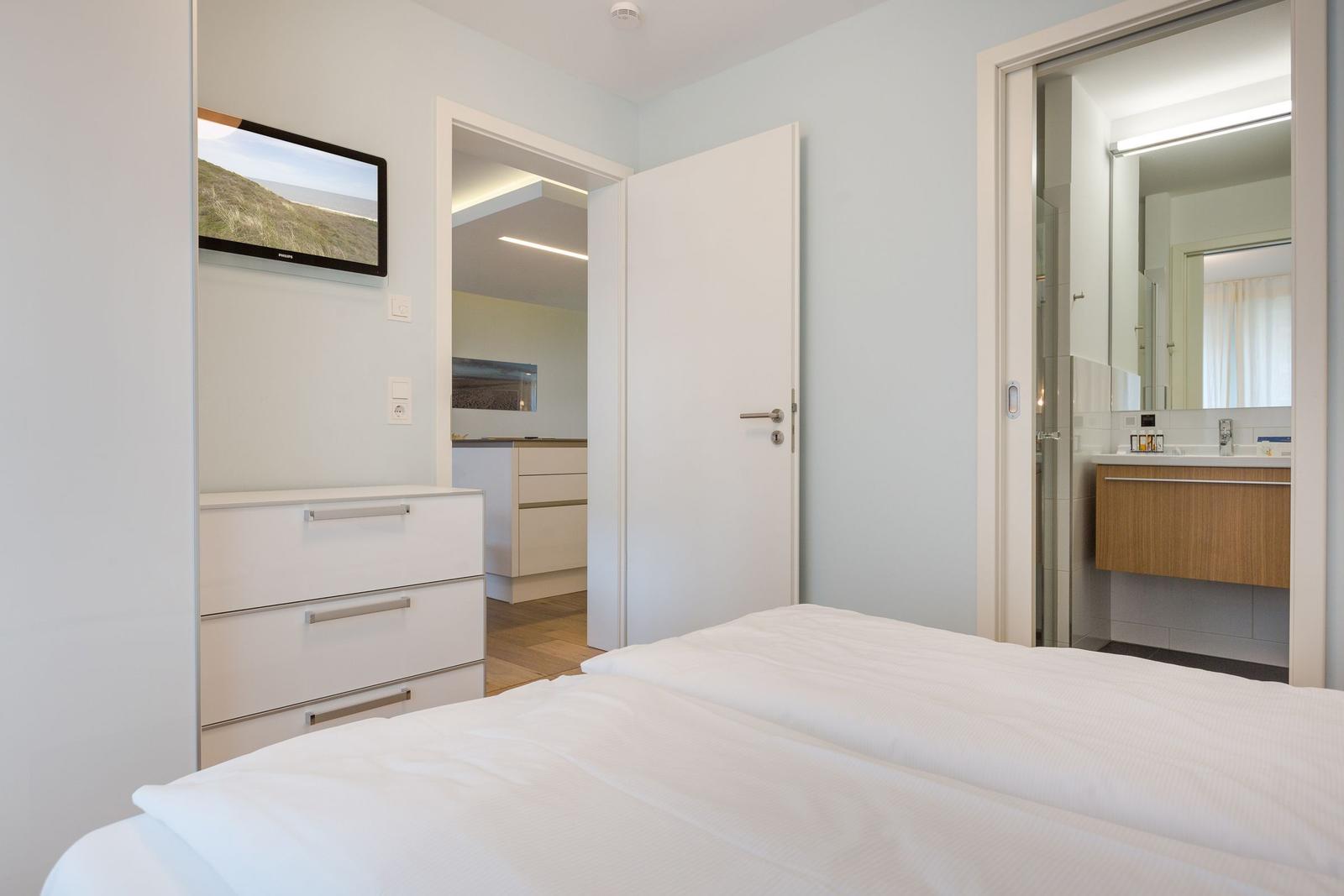 Schlafzimmer mit Bett, Schrank und TV. Blick in Küche und Bad.