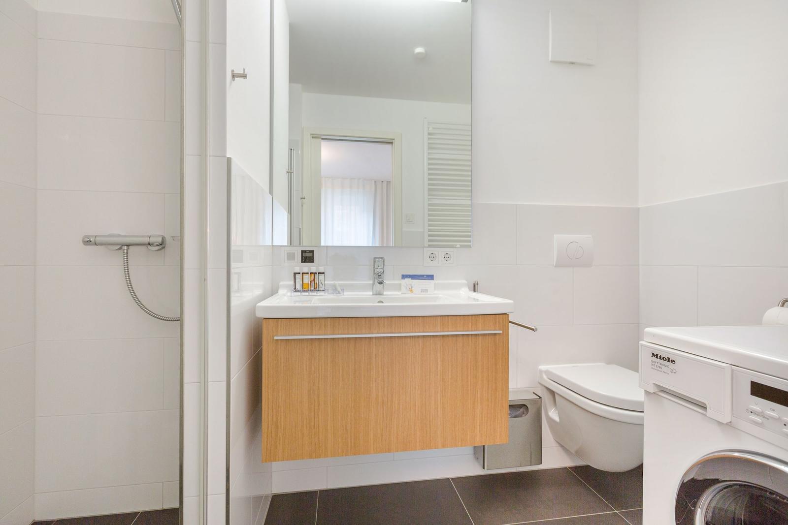 Badezimmer mit Waschbecken, Dusche, Toilette und Waschmaschine.