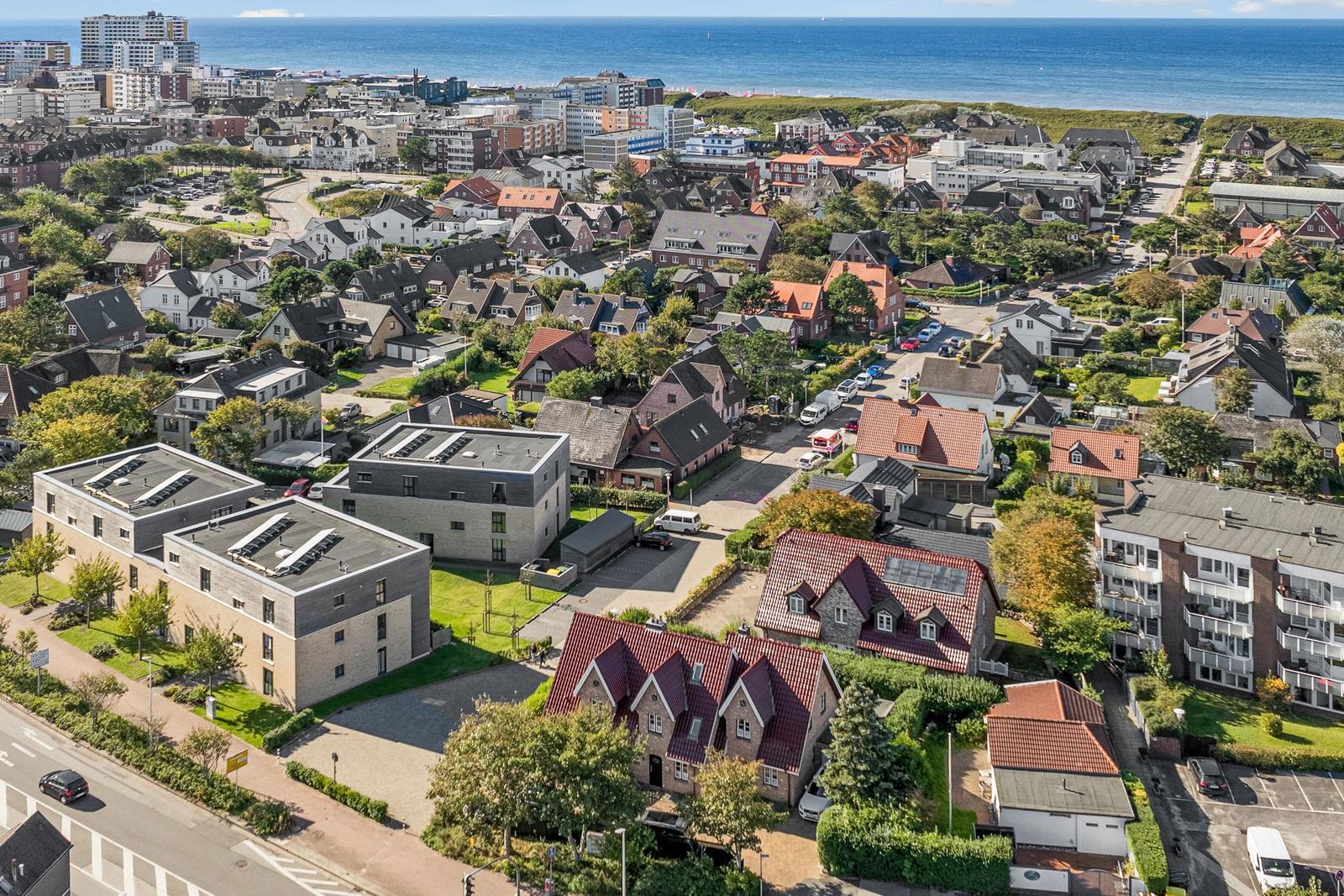 Aerial view of coastal town with houses, greenery, and ocean in background.