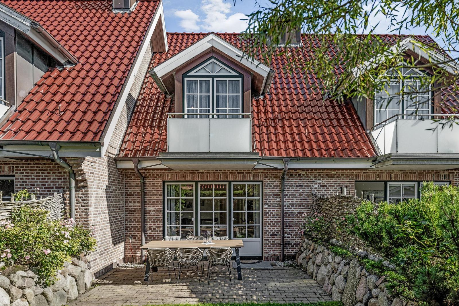 Haus mit rotem Dach, Terrasse und Gartenbereich mit Tisch und Stühlen.
