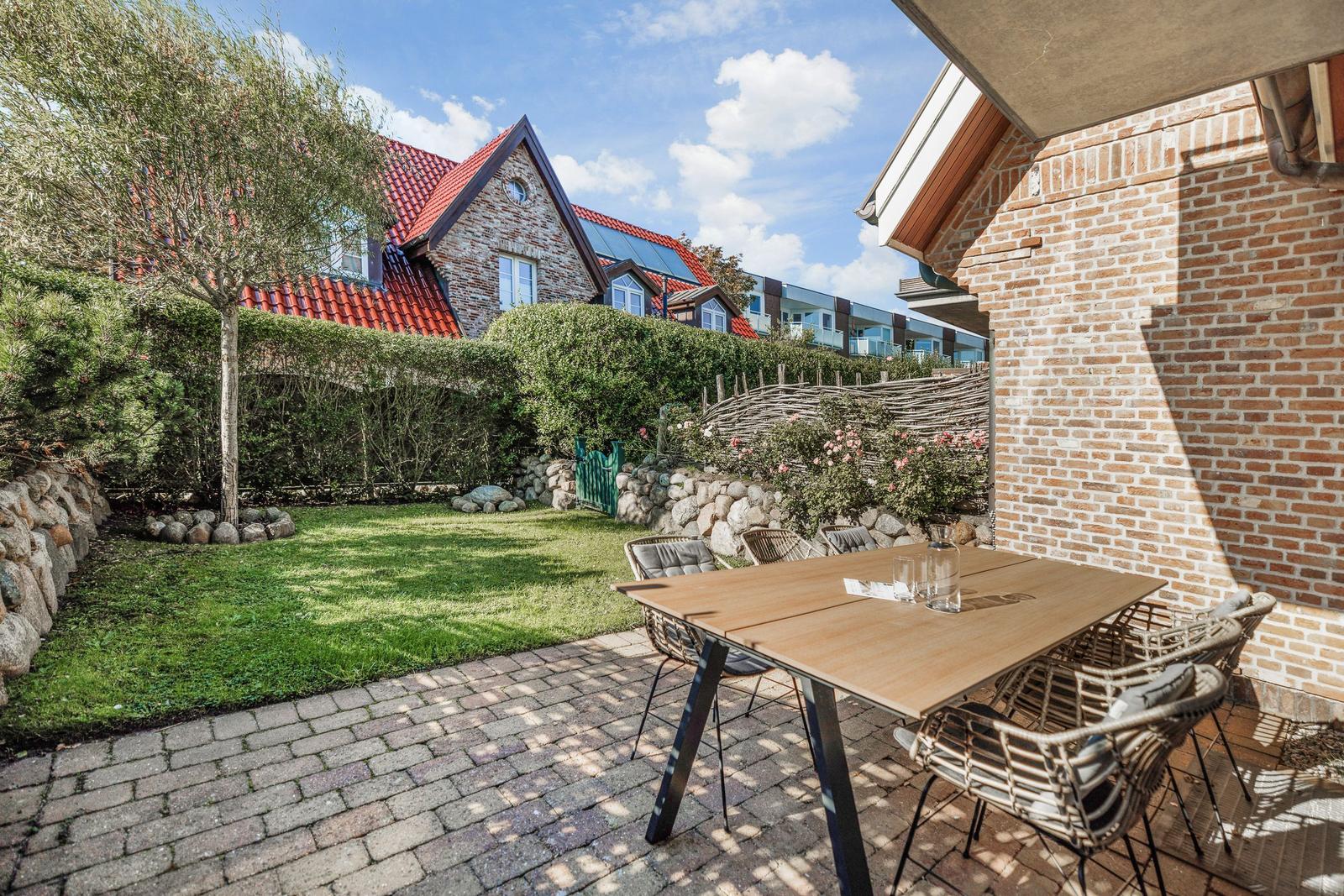 Terrasse mit Tisch und Stühlen, Grünfläche und Steinmauer im Hintergrund.
