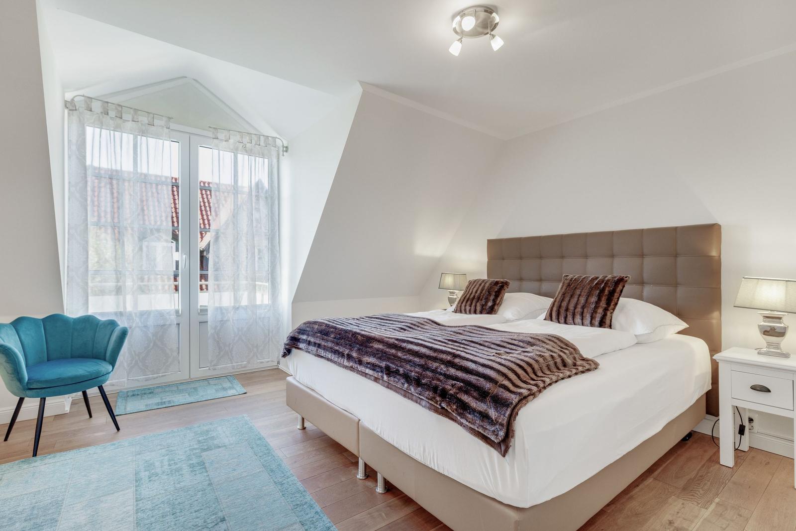 Schlafzimmer mit Doppelbett, blauer Sessel und Fenster zur Aussicht.