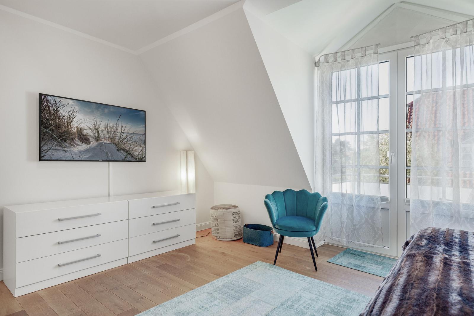 Schlafzimmer mit Dachschrägen, blauer Sessel und Fernseher an der Wand.