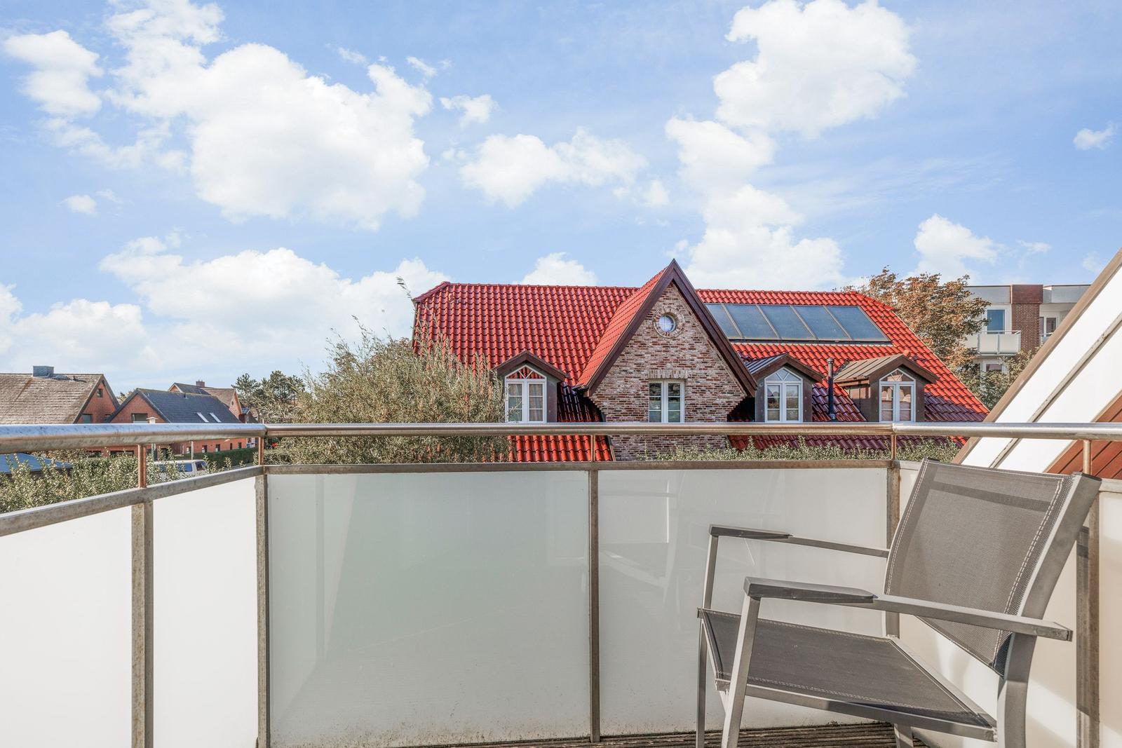 Terrasse mit Sitzgelegenheit und Blick auf ein Haus mit rotem Dach.