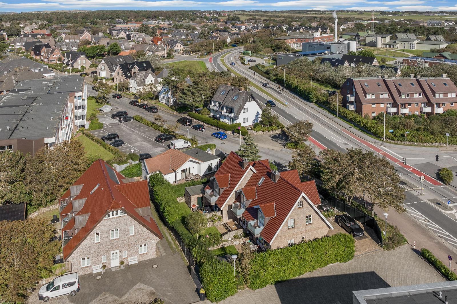 Haus mit rotem Dach und Garten, umgeben von Wohnhäusern und einer Straße.