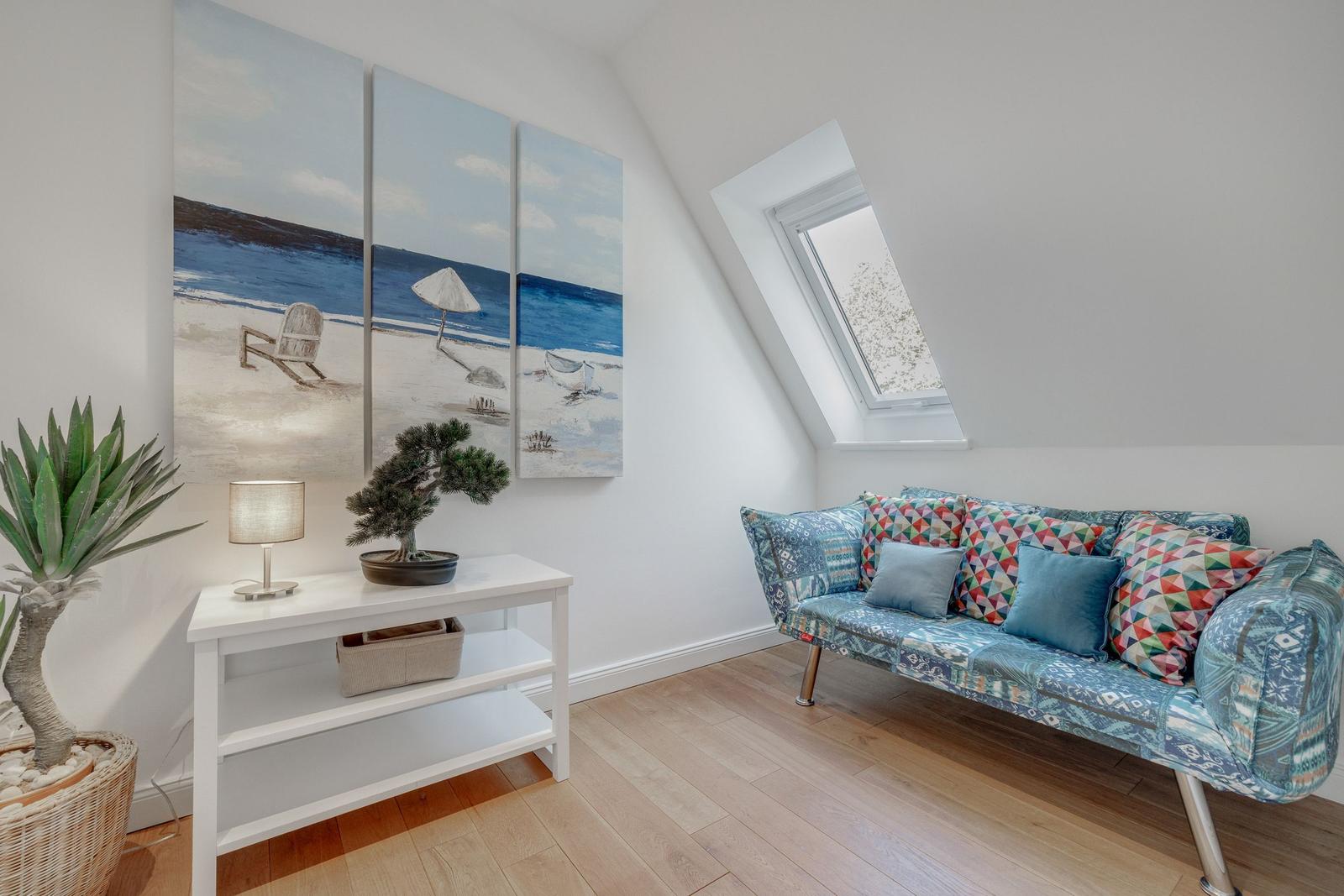 Dachgeschosszimmer mit Sofa, Fenster und Wandbildern