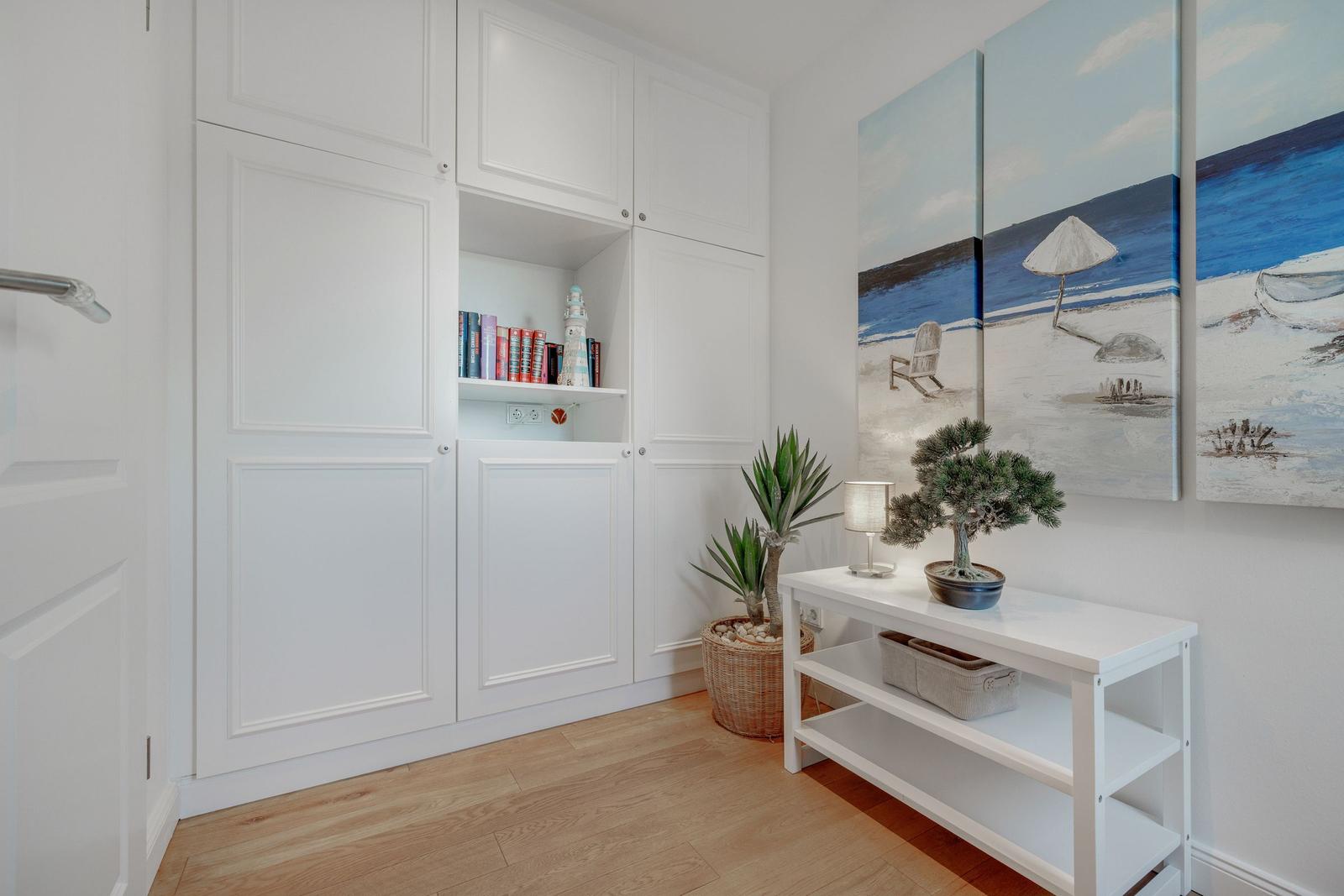 Wohnbereich mit weißen Schränken, Bonsai, Pflanze und Strandgemälde an der Wand.