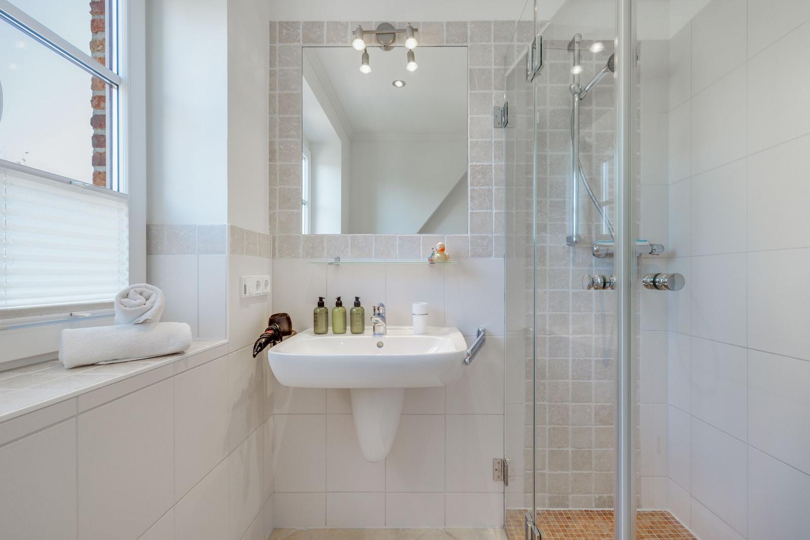 Badezimmer mit Dusche, Waschbecken und Fenster mit Handtüchern.