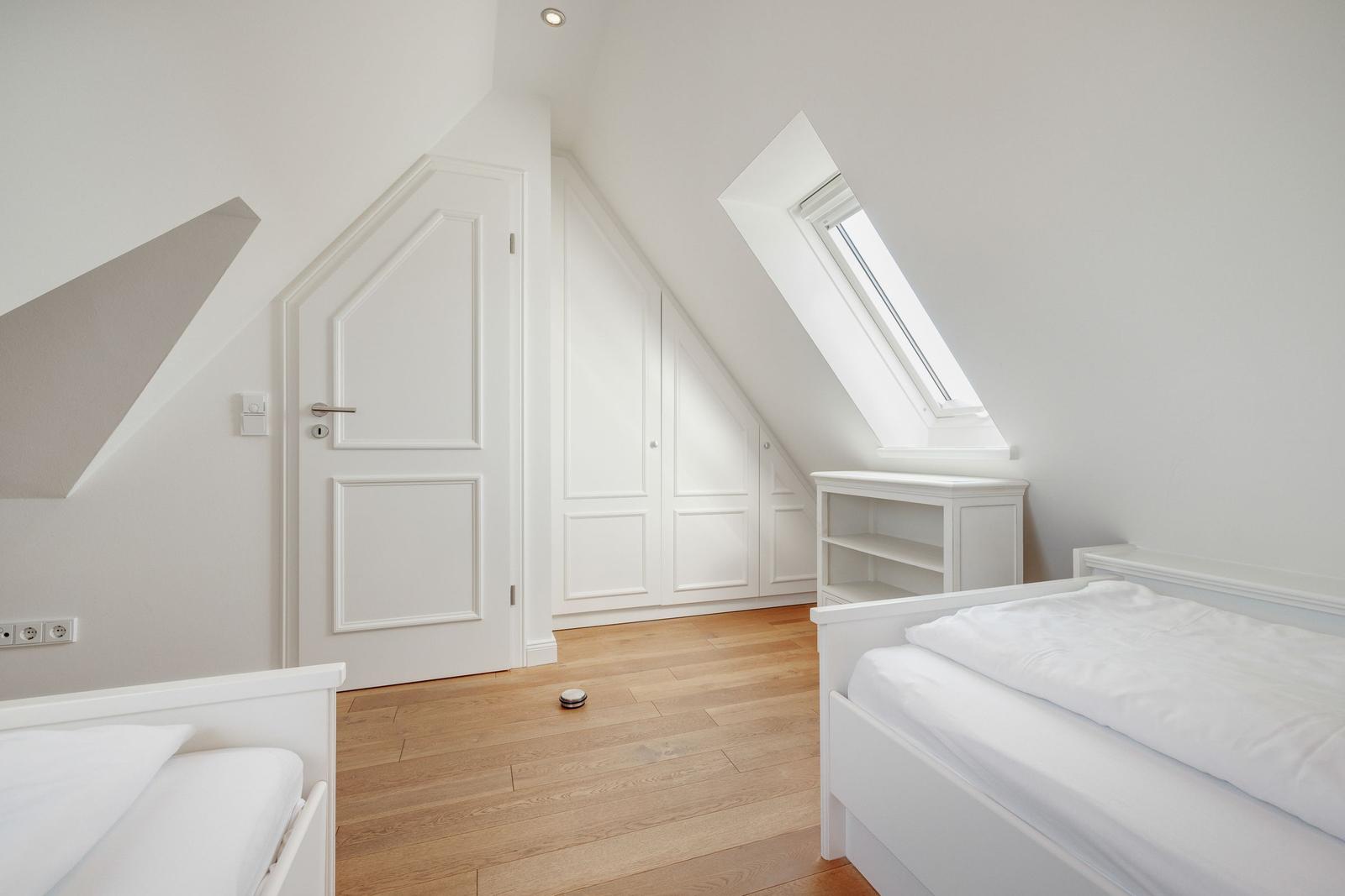 Zimmer mit zwei Betten, Dachschrägen, Fenster und Holzboden.