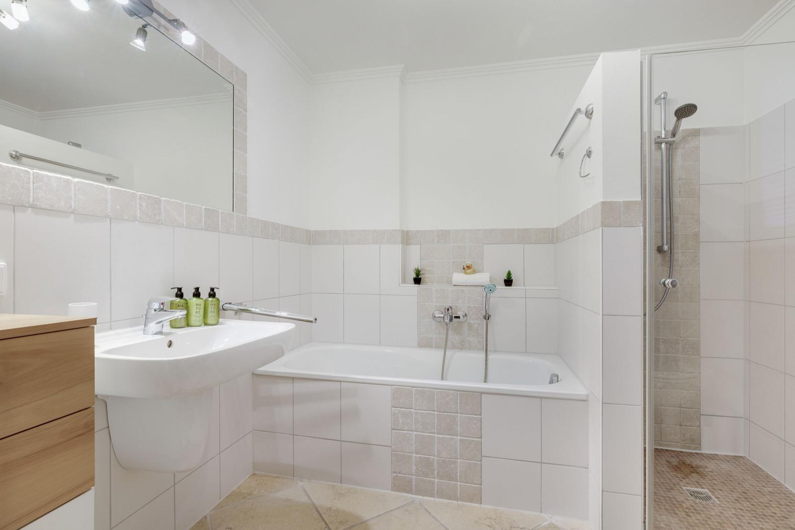 Badezimmer mit Badewanne, Dusche und Waschbecken mit Spiegel.
