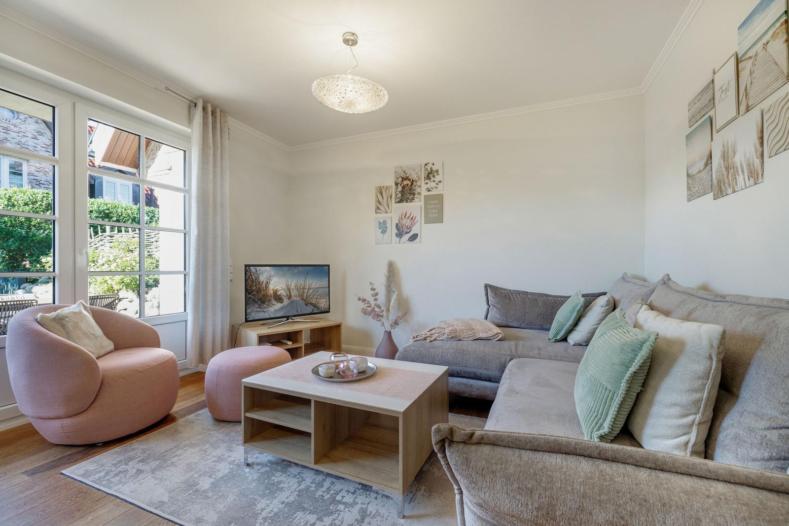 Wohnzimmer mit Sofa, Sessel und TV. Fenster mit Blick auf Garten.