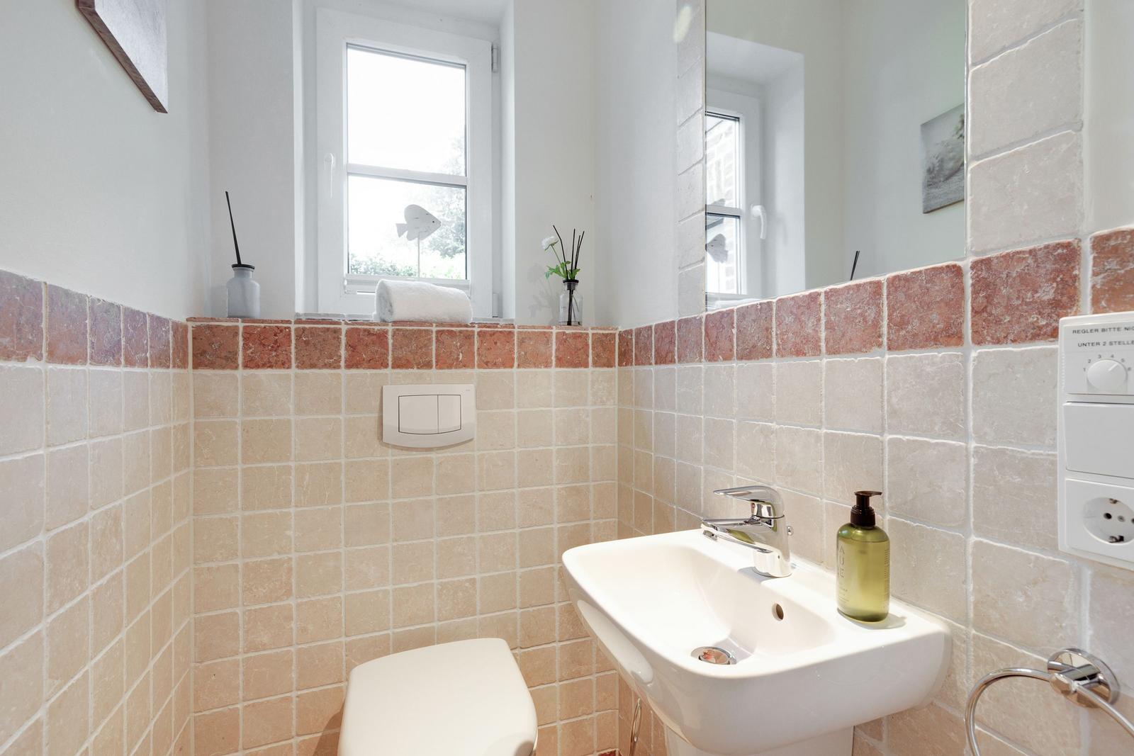 Bathroom with sink, toilet, and window. Wall cladding made of stone tiles.