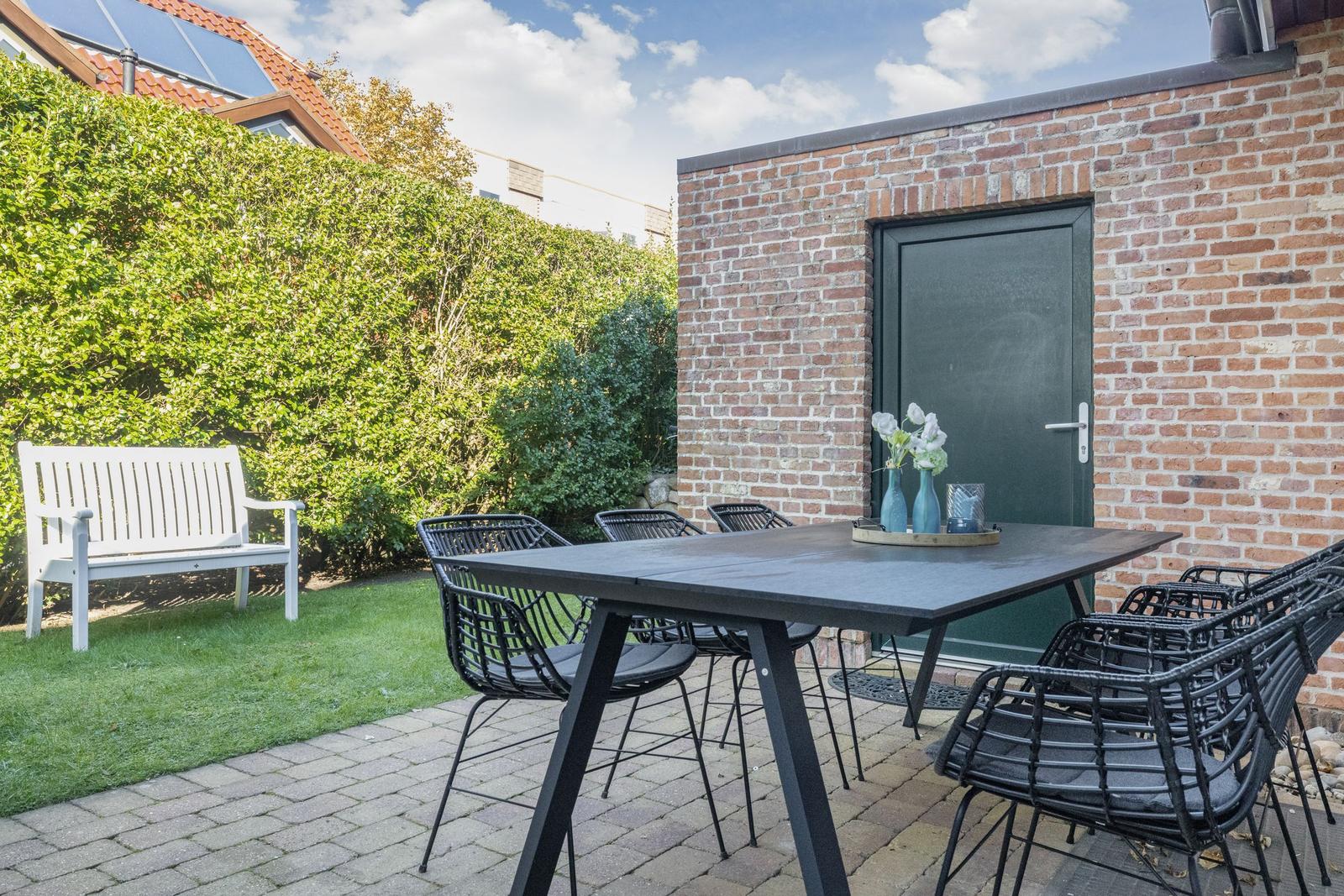 Outdoor area with table, chairs, and white garden bench against brick wall.