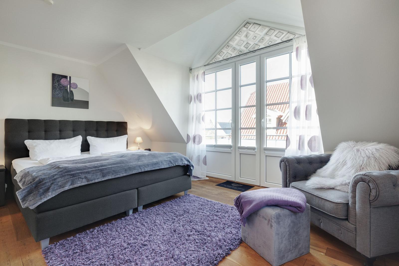 Bedroom with bed, sofa, and window. Wooden floor and purple rug.