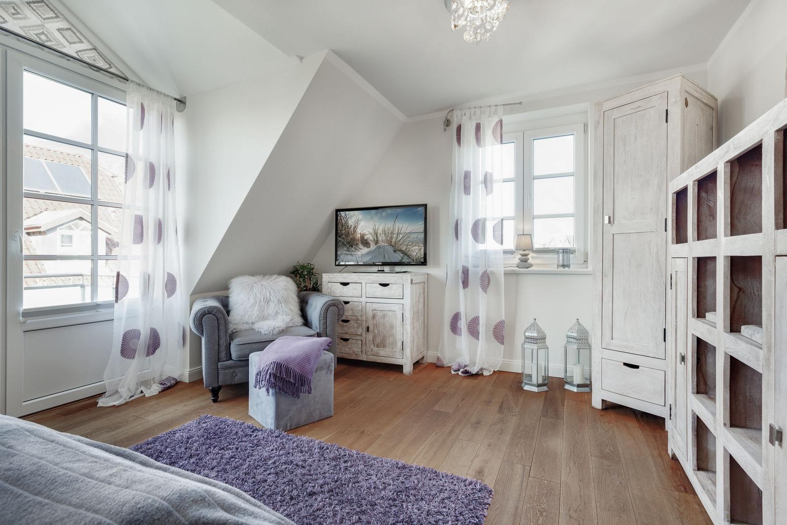 Bedroom with sloped ceiling, TV, gray armchair, and wooden floor.