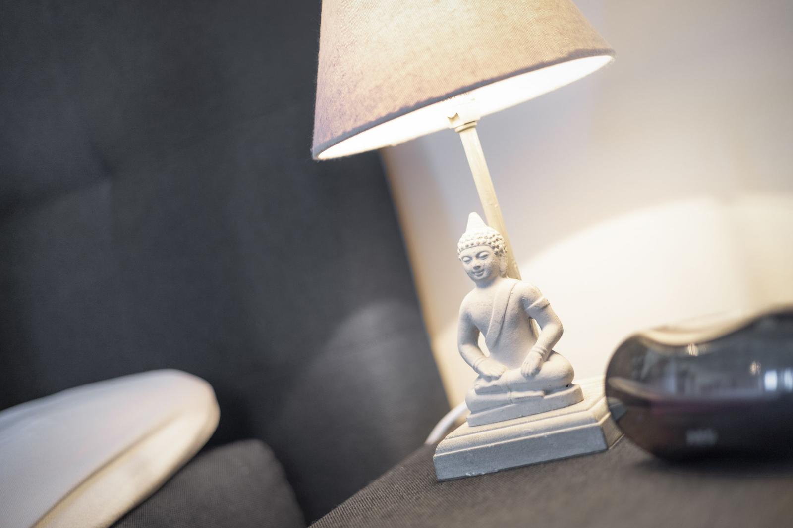 Table lamp with Buddha figurine on dark furniture piece.
