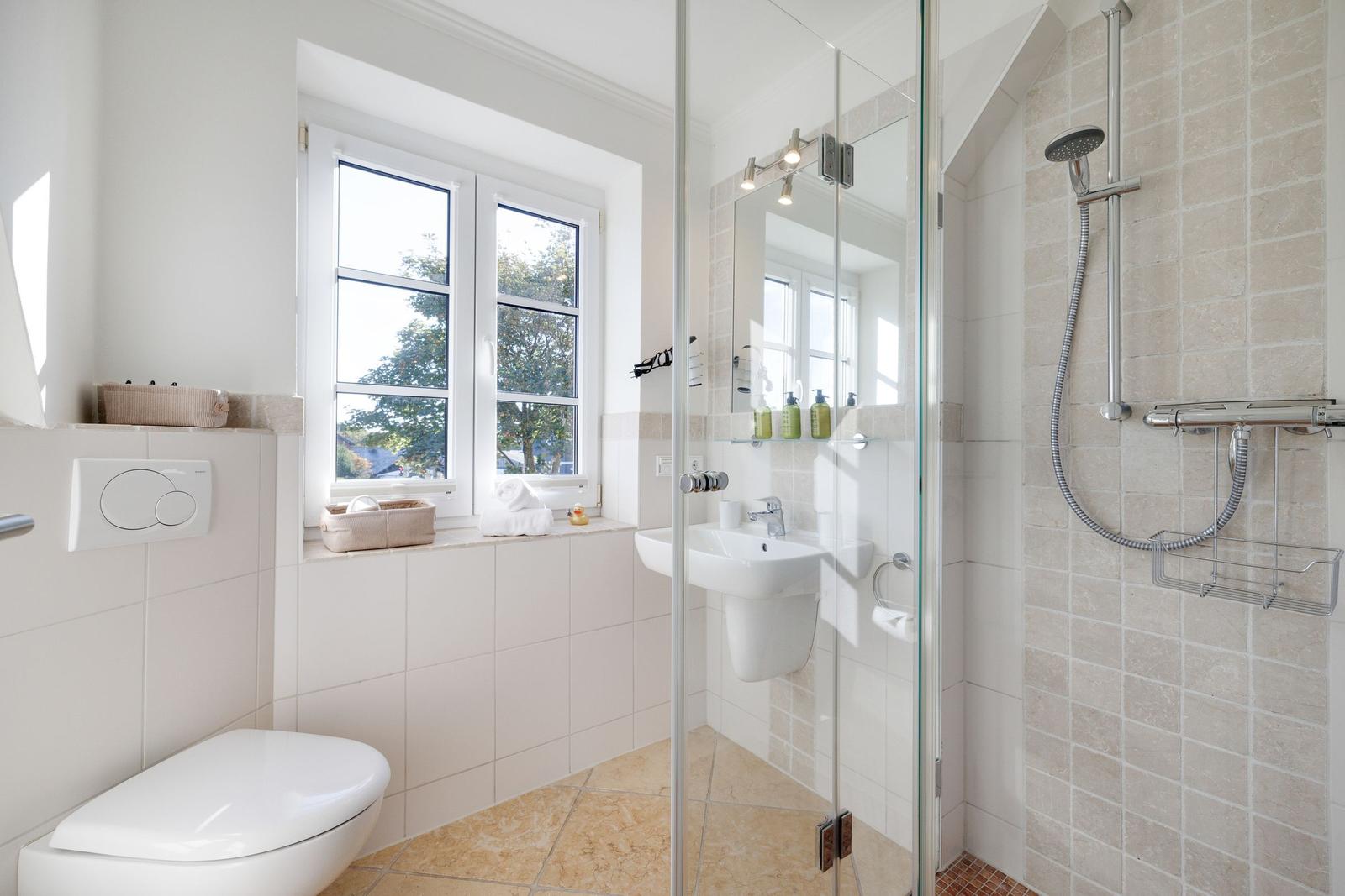 Bathroom with shower, sink, and toilet. Window with view of greenery.