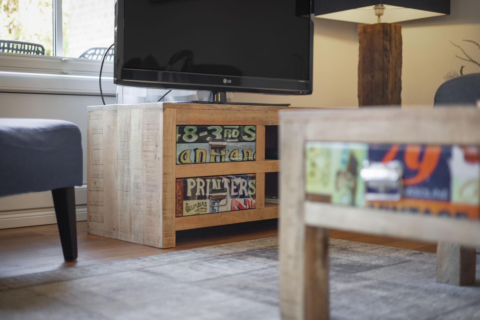 TV on wooden console with stickers, beside table and chair.