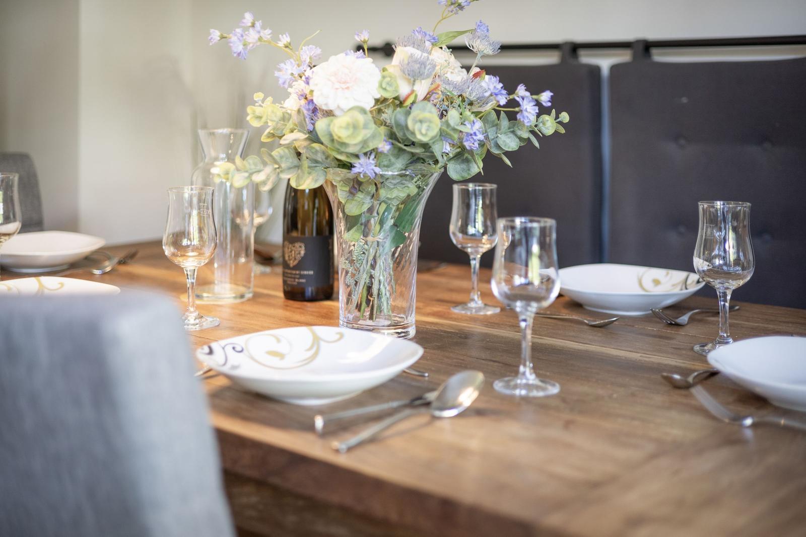 Wooden table with set places and flower vase in the middle.